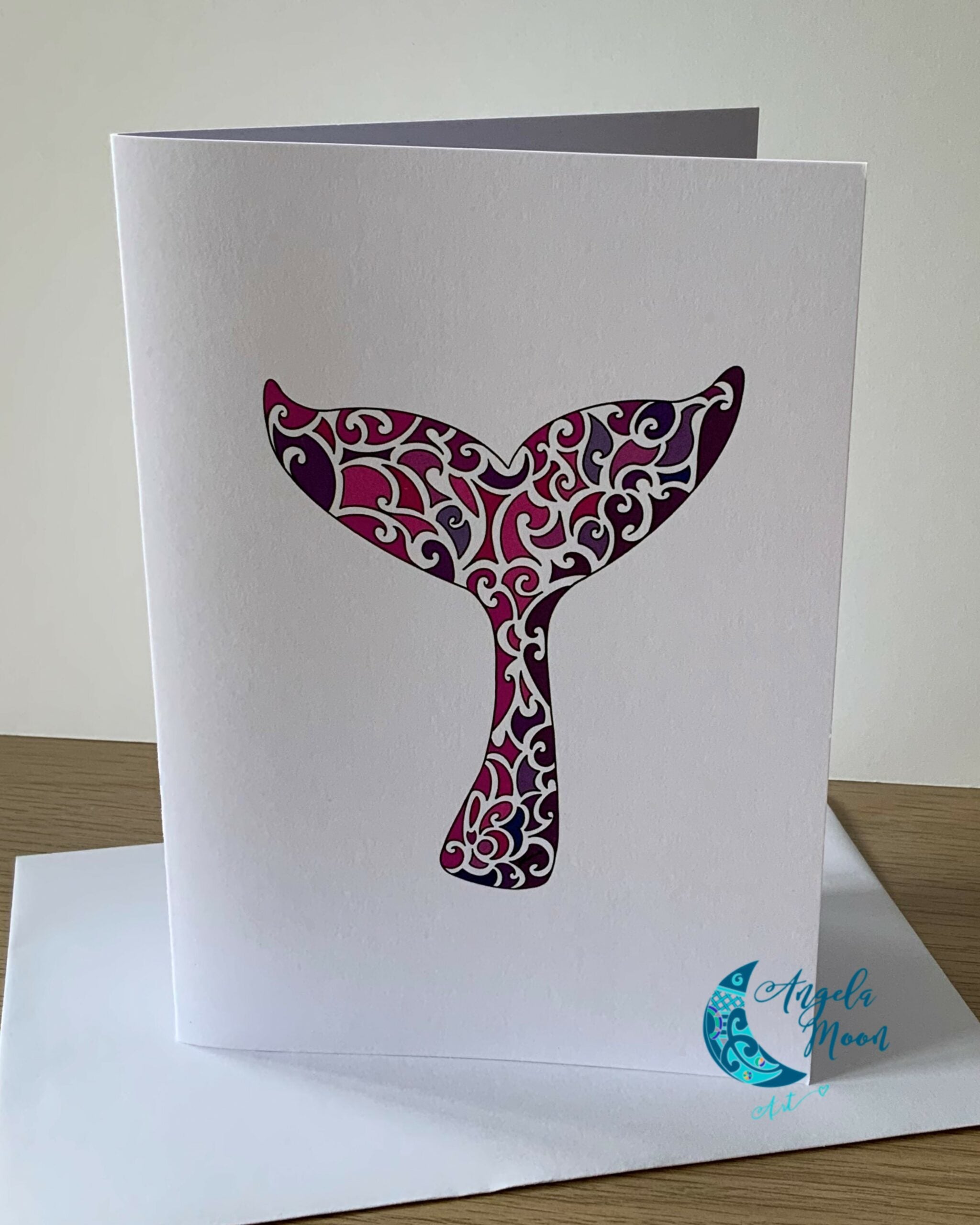 Elegantly designed Pink Whale Tail Card, a product of Angela Moon Art, with a cut-out of a whale tail, featuring intricate purple and pink swirl patterns, accompanied by the artist's signature at the bottom right