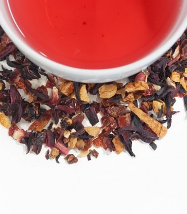 A vibrant cup of the Strawberry Kiwifruit Tea Tagalong by Harney & Sons surrounded by scattered loose-leaf herbal blend on a white background.