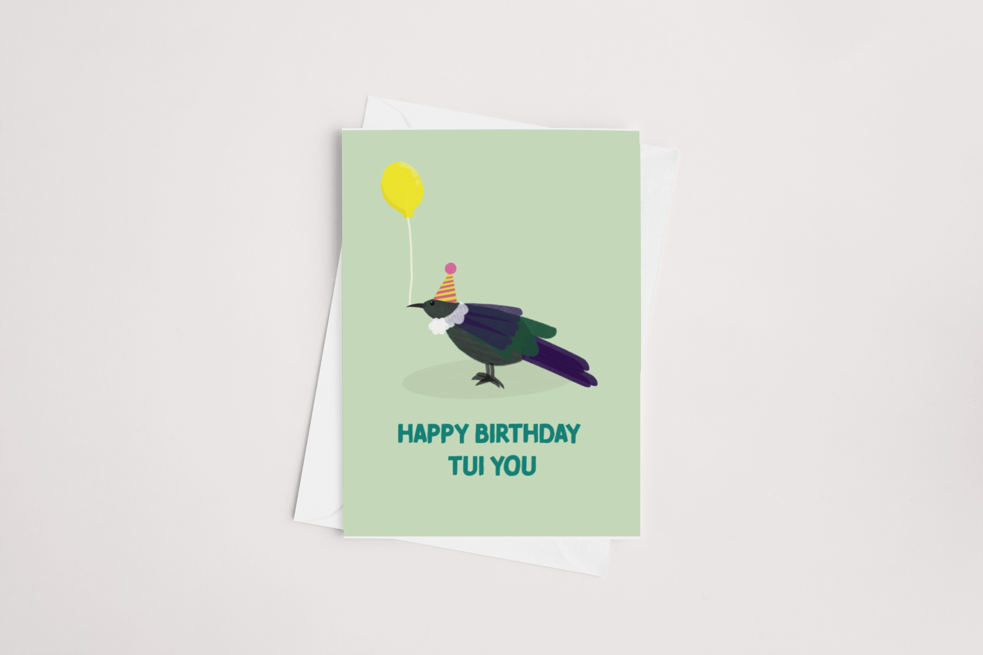 A whimsical Tui Birthday Card by Tuesday Print featuring a cartoon bird wearing a party hat and holding a yellow balloon, alongside the cheerful message: "happy birthday to you." Product of New Zealand.