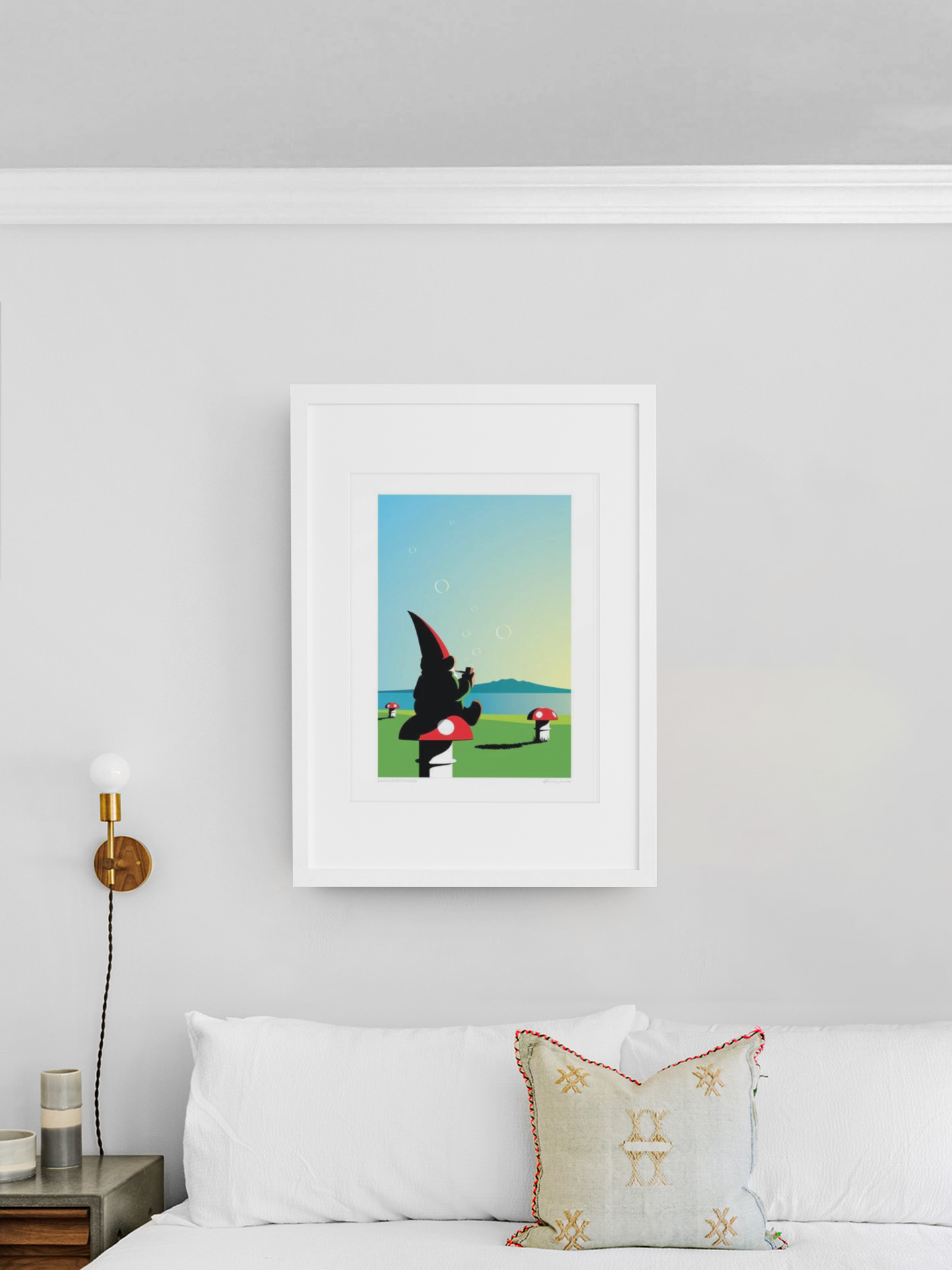 A Devonport Gnome art print by Glenn Jones hanging on a clean, white wall featuring a stylized cartoon character leaping between platforms against a sky-blue background, dotted with whimsical mushroom houses and playful local gnomes.