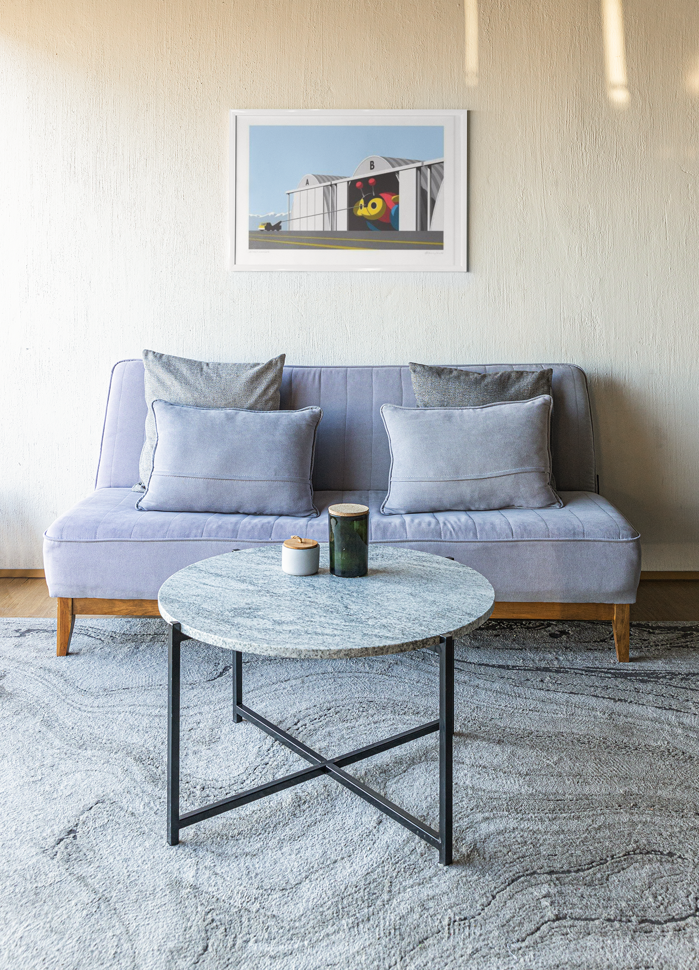 A cozy living room corner featuring a modern Secret Hangar sofa by Glenn Jones adorned with matching cushions, paired with a round, marble-top coffee table on which rest a candle and a drinking cup, all set against a clean.