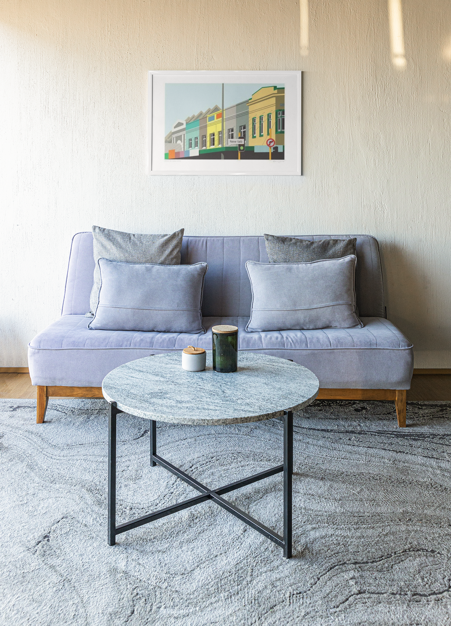 A cozy and minimalist living room setup featuring the Heart of Grey Lynn couch by Glenn Jones with plush cushions, a circular marble-top coffee table with a candle on it, all placed on a soft, textured rug. The scene is