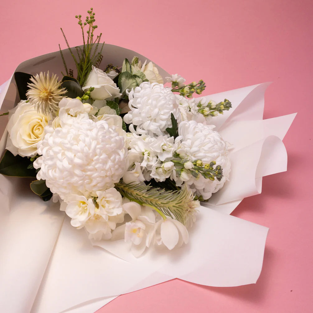 A delicate bouquet of Doreen White & Green from Poppy in April floral collections, wrapped in white paper and presented on a soft pink background.