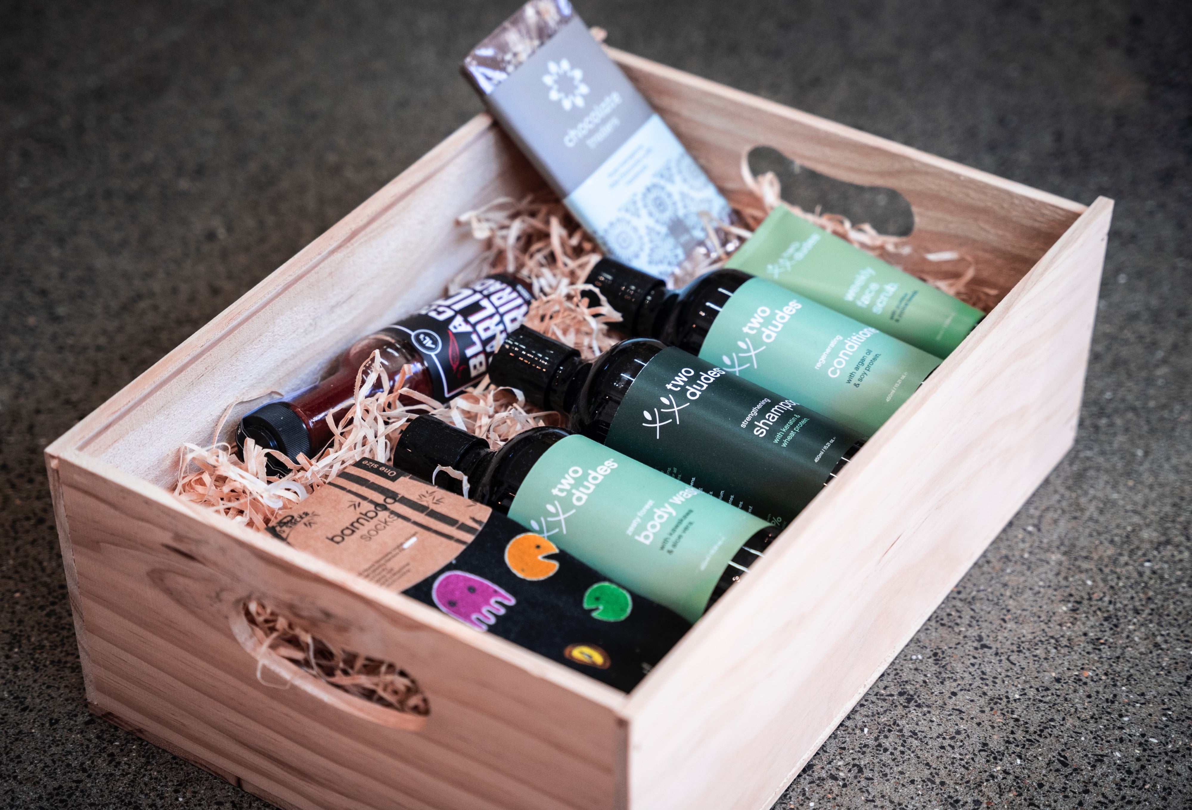 A His giftbox co. filled with various men's grooming products, including bottles and tubes, neatly arranged on a bed of straw, displayed on a gray surface.