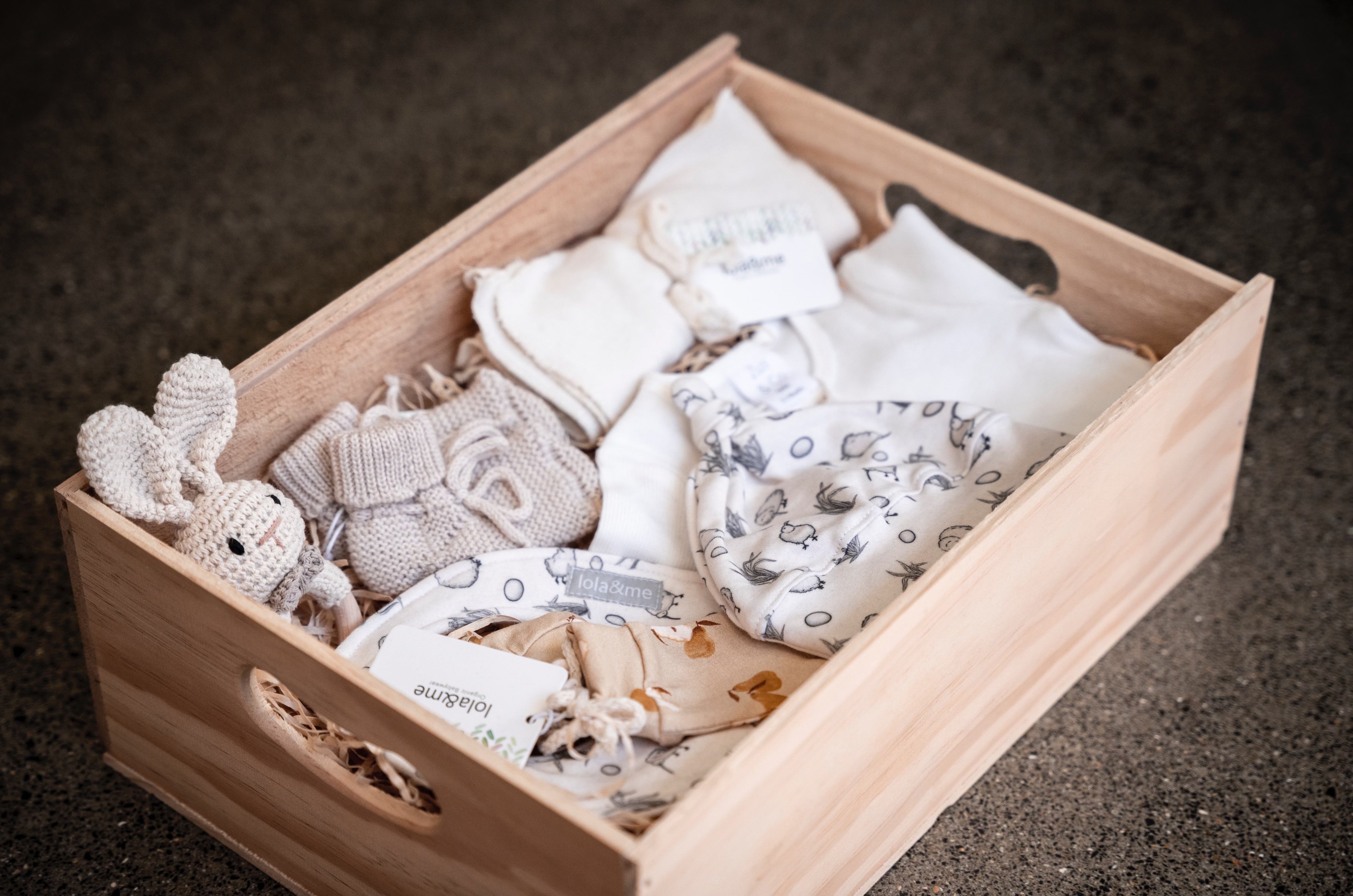 A neatly organized New Arrival baby memory box from giftbox co. filled with organic cloths and merino knit booties, cherishing the early moments of a child's life.