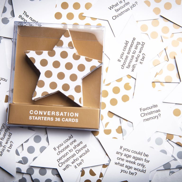 A set of Christmas Conversation Starters Cards by giftbox co. is displayed, showcasing gold and silver polka dot designs ideal for a festive Christmas gathering. These cards pose questions such as "What is your favourite Christmas memory?" and are packaged in a star-shaped box labeled "Conversation Starters 36 Cards.