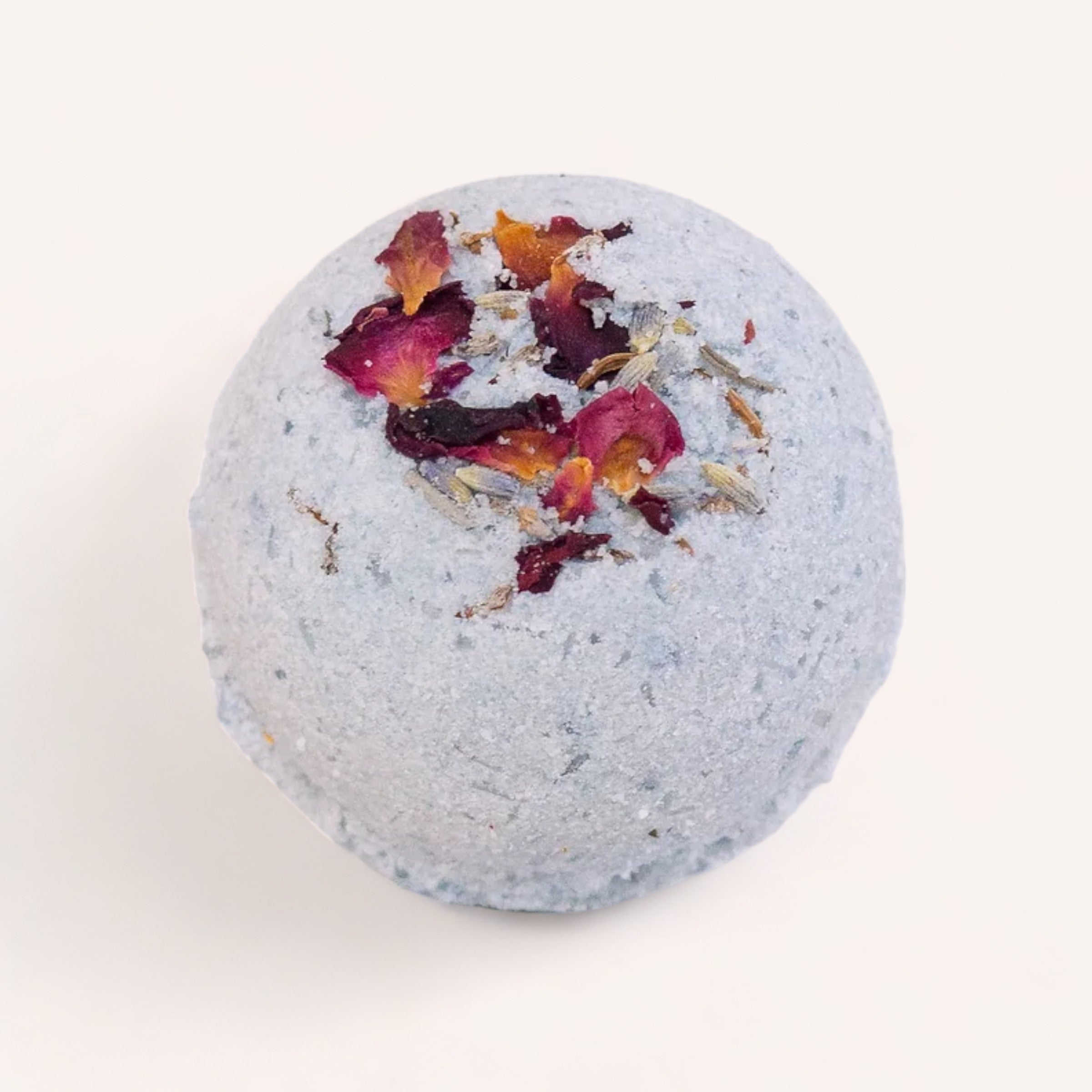 A single Midnight Garden Bath Bomb by Botanical Skin Care with dried petals on a white background.