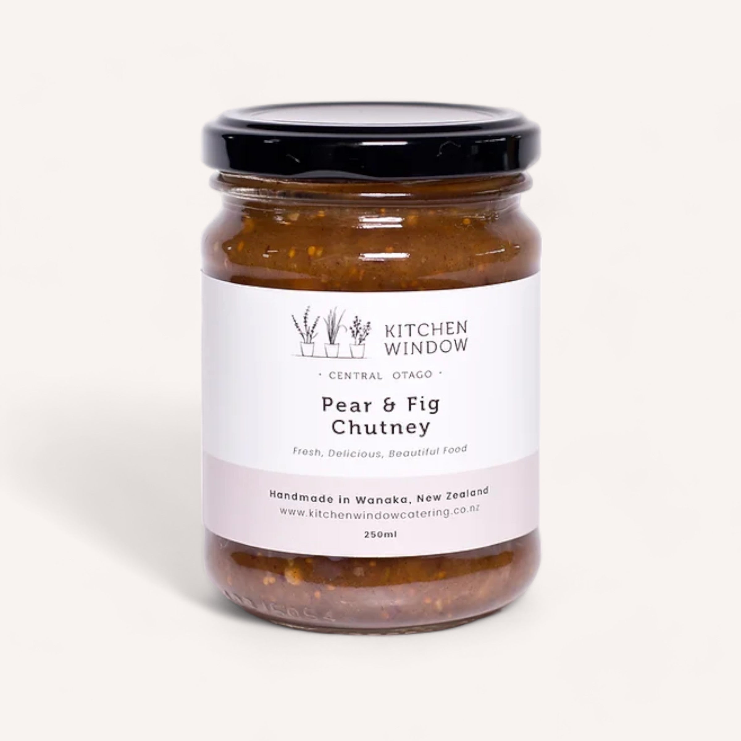 A 250ml jar of Pear & Fig Chutney by Kitchen Window, an ideal accompaniment for a cheese board, is handcrafted in Wanaka, New Zealand. It features a black screw-on lid and an elegant white label showcasing "Fresh, Delicious, Beautiful Food." This product has been recognized at the NZ Artisan Awards.