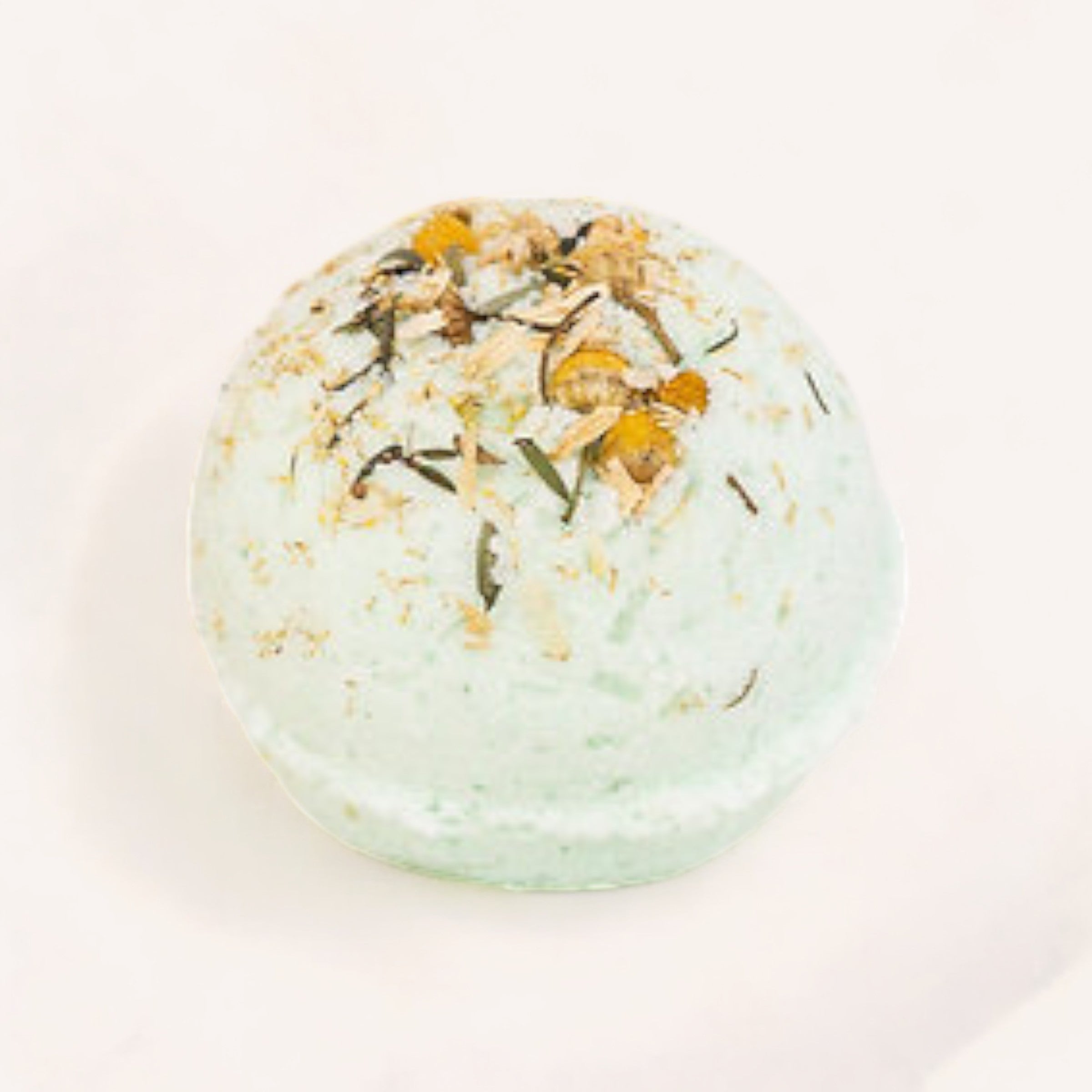 A fresh, natural fizzing Mint, Manuka & Chamomile Bath Bomb with dried flower petals on a light background by Botanical Skin Care.