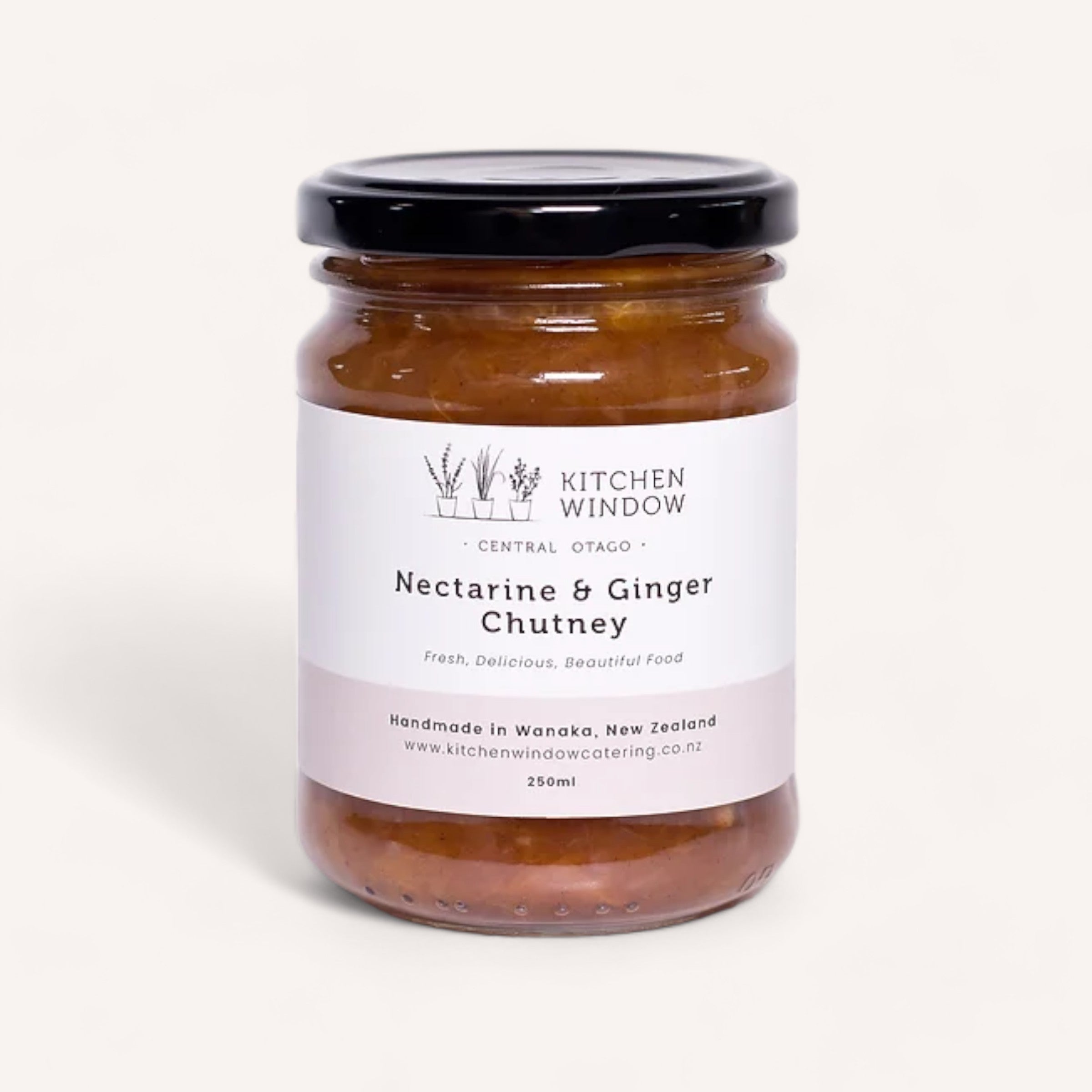 A 250ml jar of Nectarine & Ginger Chutney by Kitchen Window, adorned with a distinctive black lid. The sophisticated white label, featuring black text, emphasizes "Central Otago" and "Handmade in Wanaka, New Zealand." This chutney, recognized at the NZ Artisan Awards, beautifully embodies the essence of exquisite nectarines.