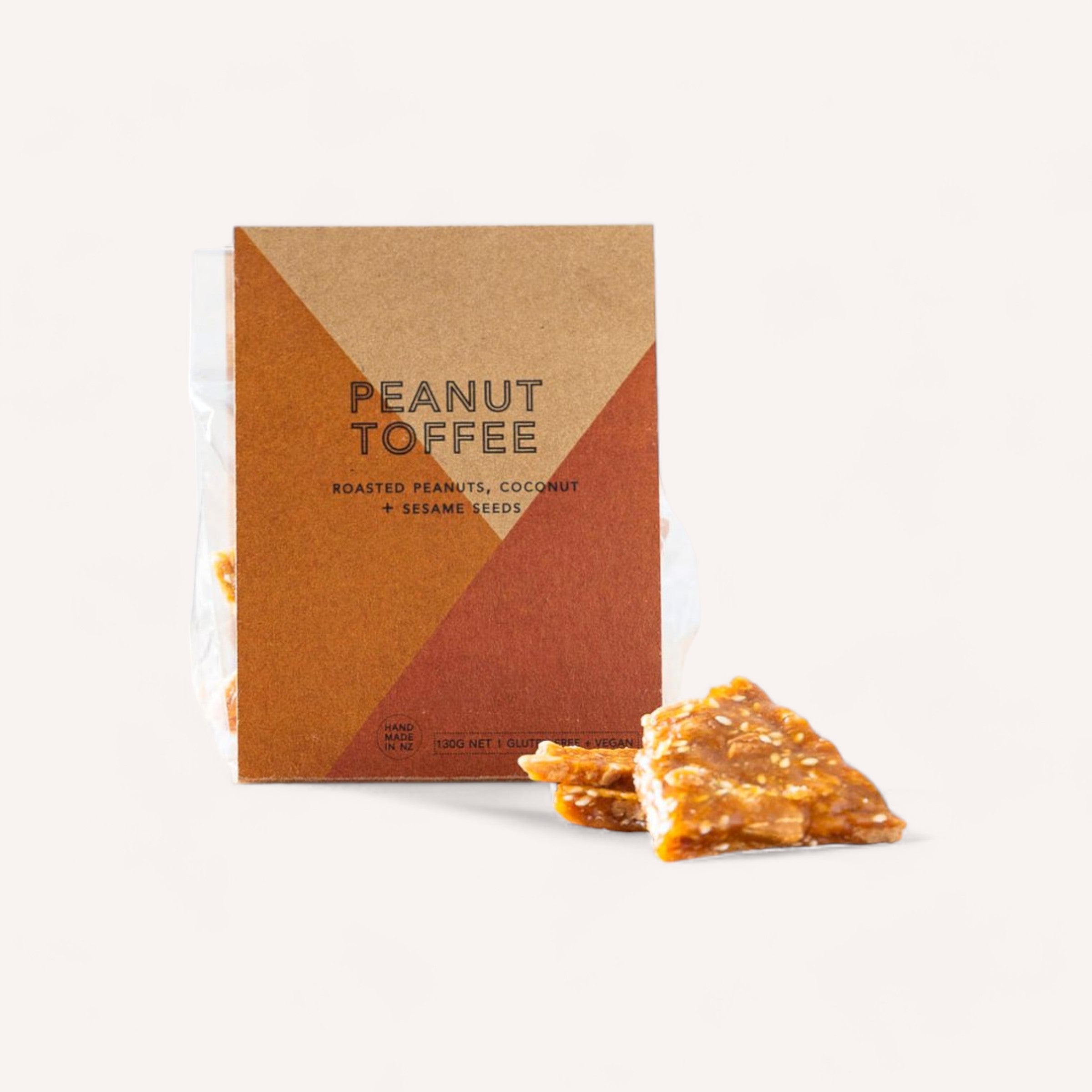 A package labeled "Peanut Toffee by Asian Food Republic" featuring oven-roasted peanuts, coconut, and sesame seeds is displayed. The brown packaging adorned with geometric designs complements the arrangement of several pieces of peanut toffee in front, highlighting their texture and nutty appearance.