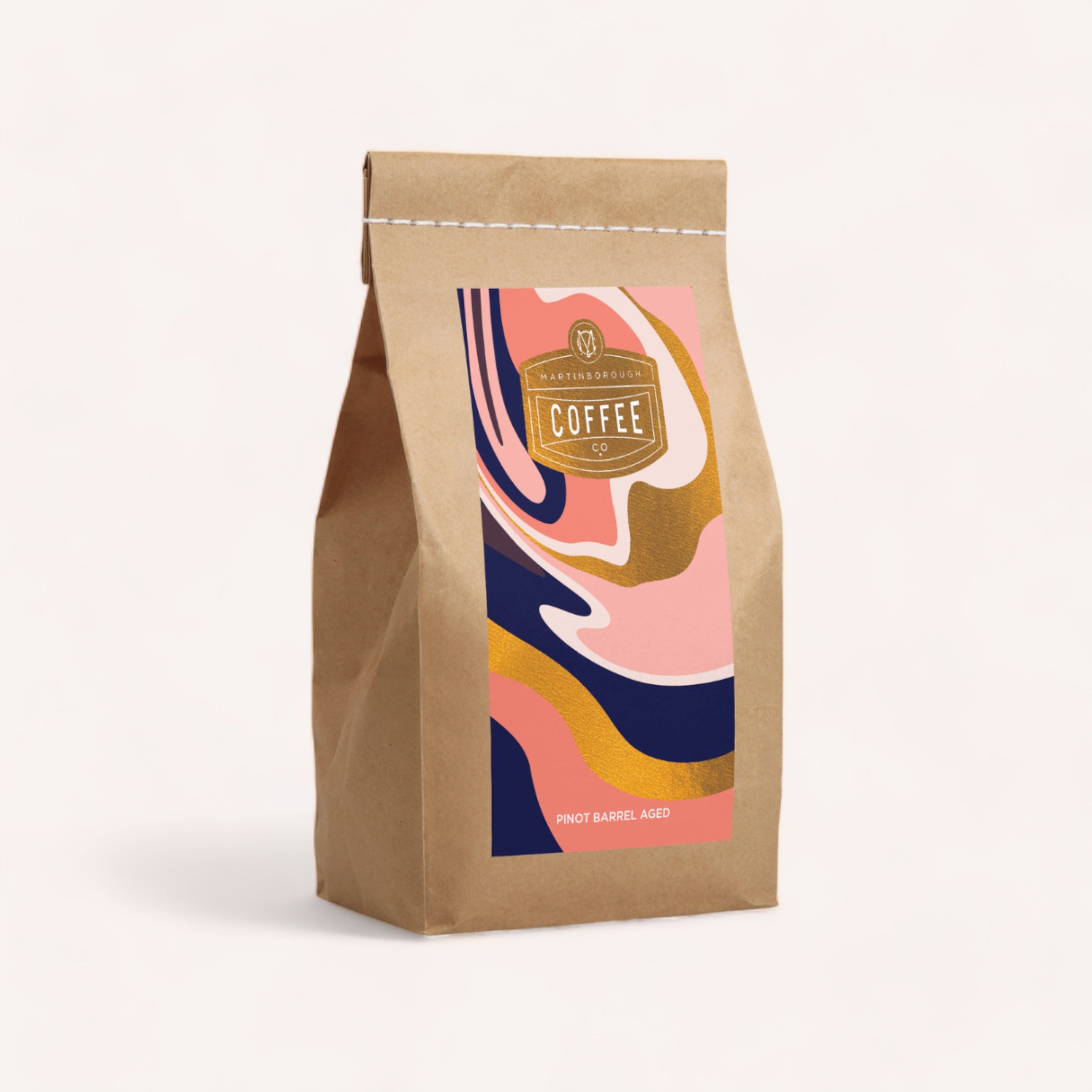 A sealed brown paper Coffee, Anyone? bag with a colorful wavy design and a label indicating "Martinborough pinot aged" coffee.