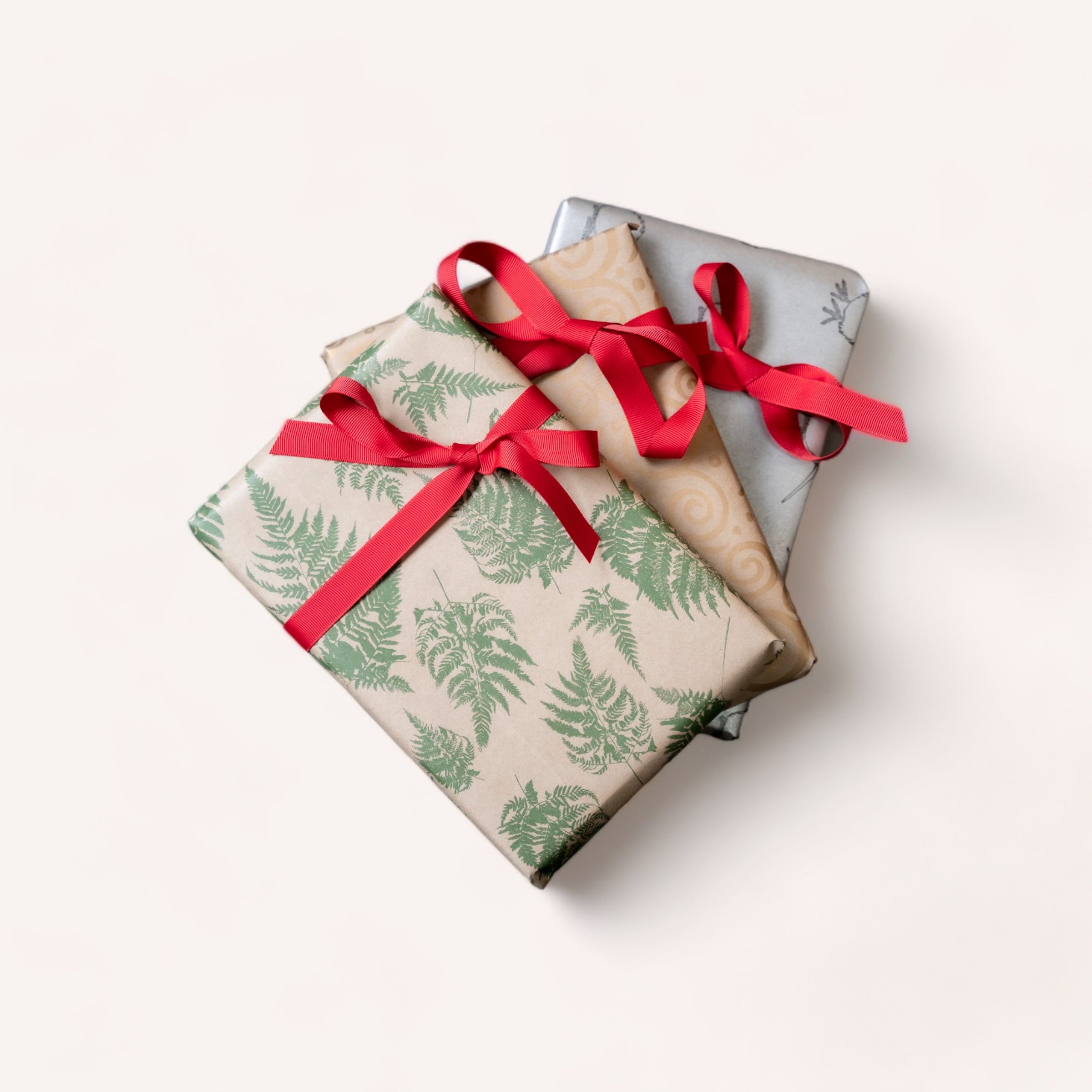 Two neatly wrapped gift boxes with red ribbons, one with fern patterns and the other with an elegant design on premium 65gsm paper, set against a clean white background.