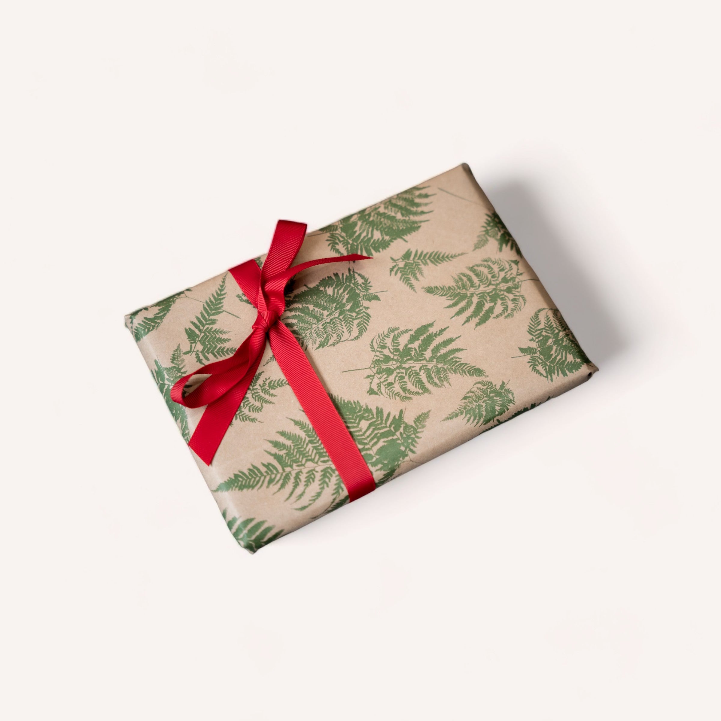 A neatly wrapped gift with fern patterned premium 65gsm giftbox co. paper and a red ribbon on a white background.