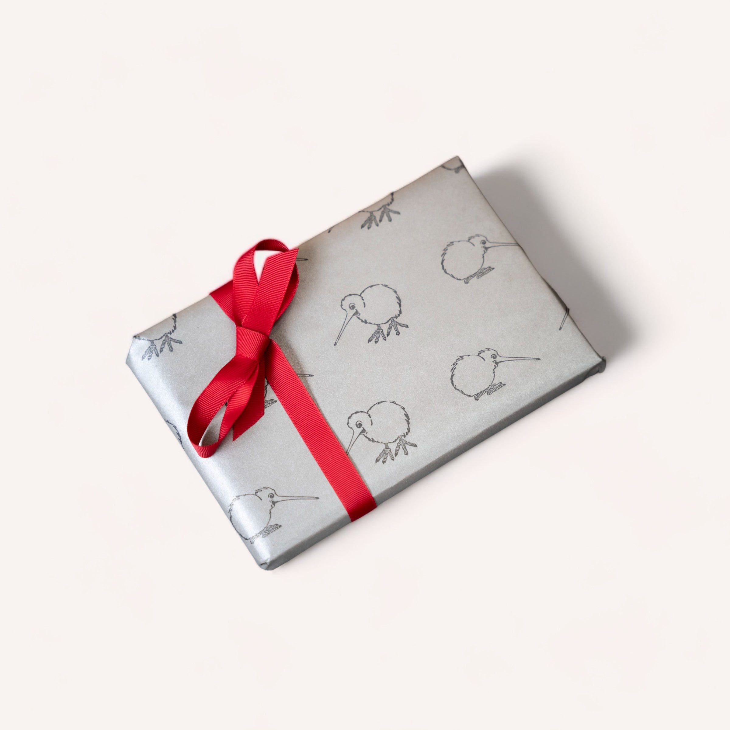 A neatly wrapped gift with a red ribbon on a simple background, showcasing a pattern with whimsical line-drawn birds on premium 65gsm giftbox co. paper.