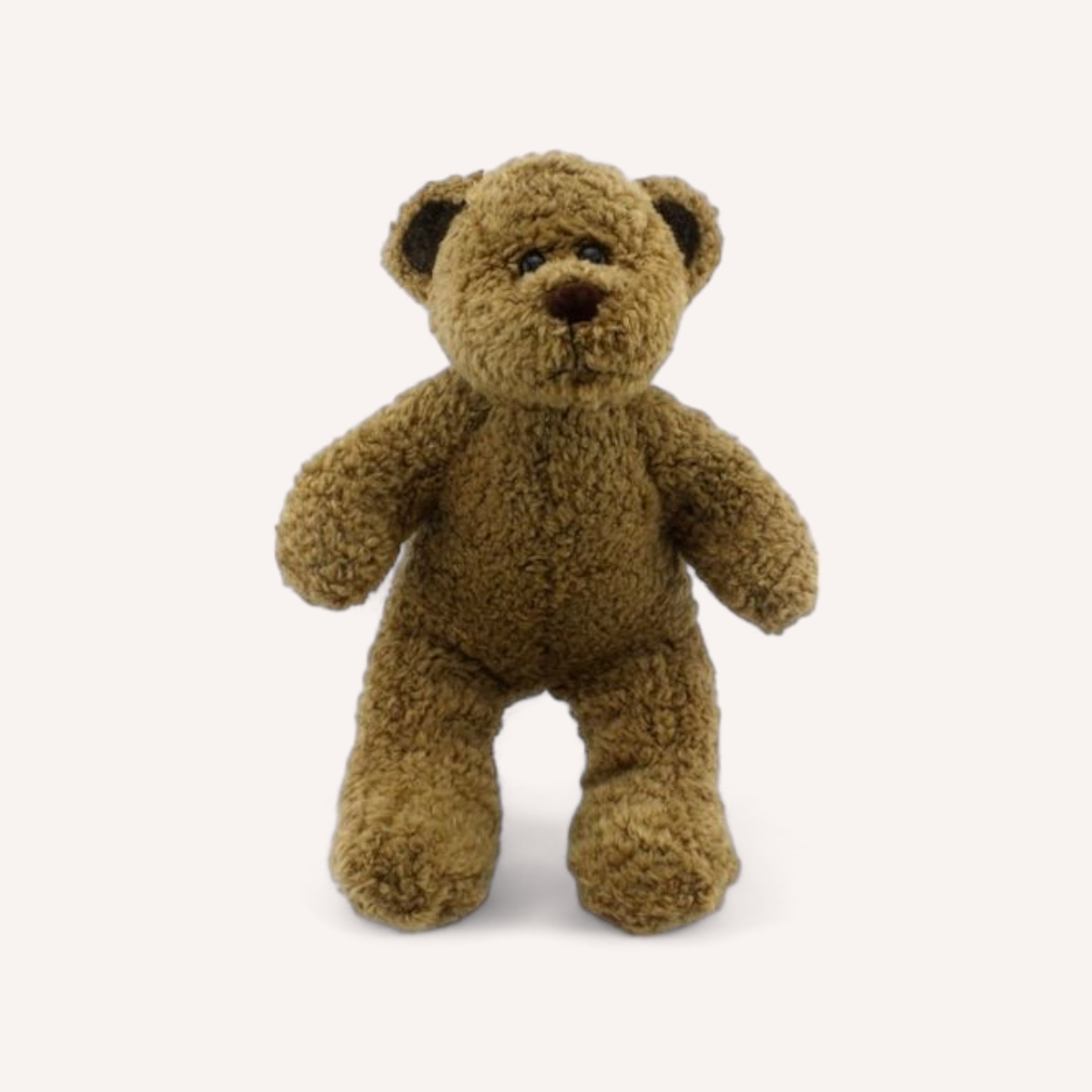 The Scruffy Bear from The Teddy Factory stands upright against a plain white background. Its round dark eyes, small brown snout, and slightly floppy ears deliver an irresistible cuddly charm. The textured fur enhances its cozy and endearing look, making it the perfect companion for comfort.