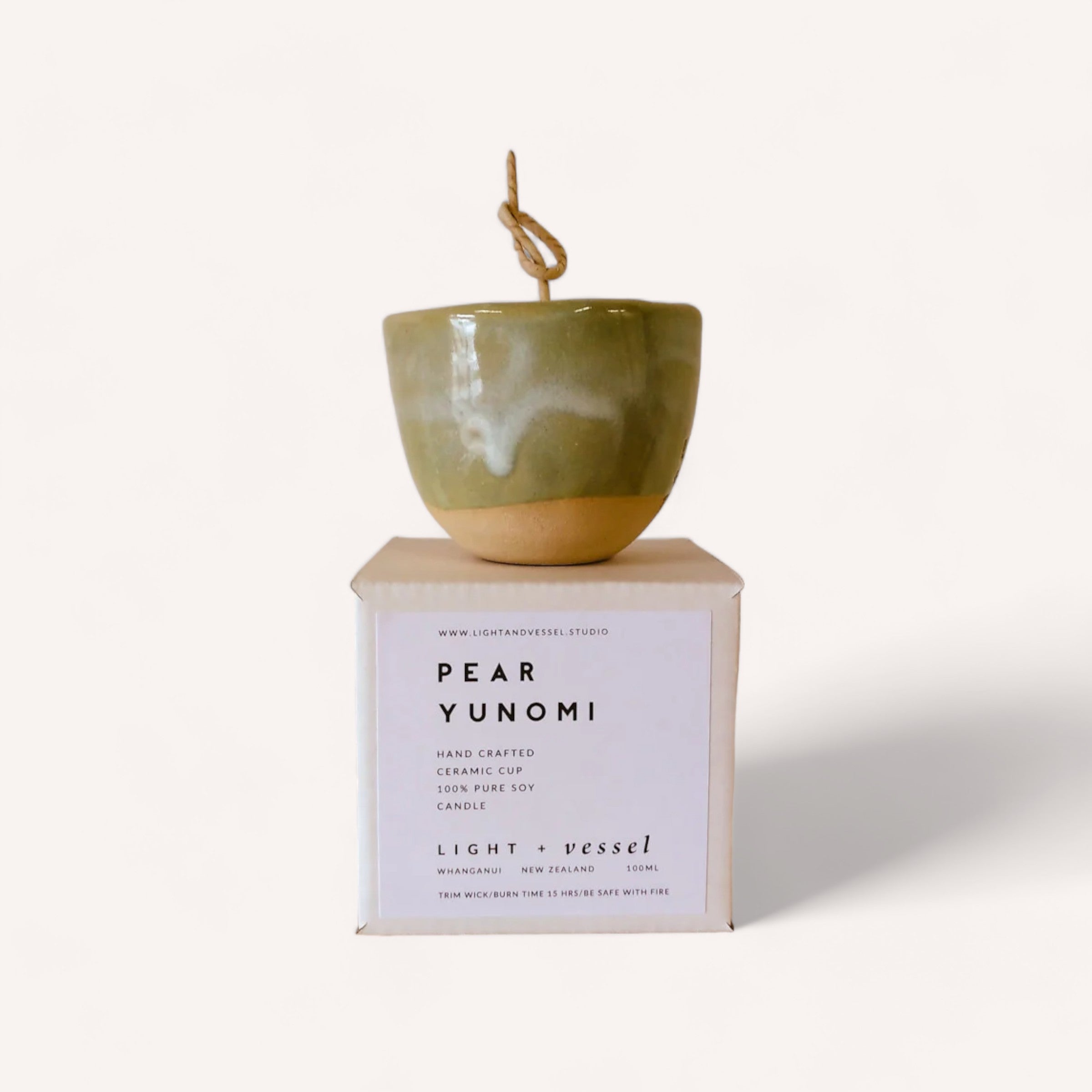 Handcrafted ceramic yunomi teacup elegantly displayed on its packaging, boasting an earthy green glaze with a rustic aesthetic, now accompanied by a Pear Candle by Light + Vessel to enhance the ambiance.