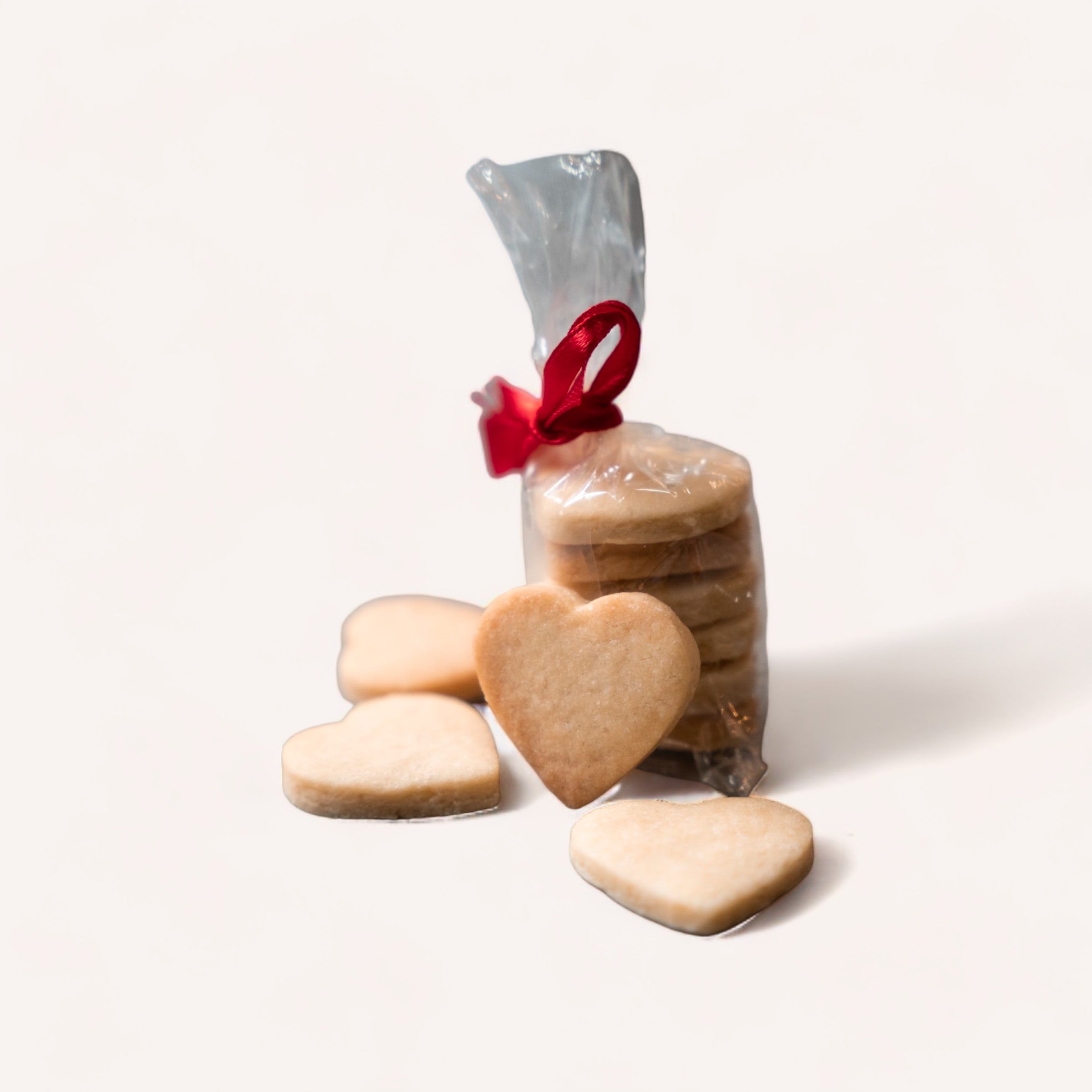 A bag of The Cookie Collective's Heart Cookie Bites tied with a red ribbon, with several cookies beside it, against a white background, makes for a heartfelt gift.