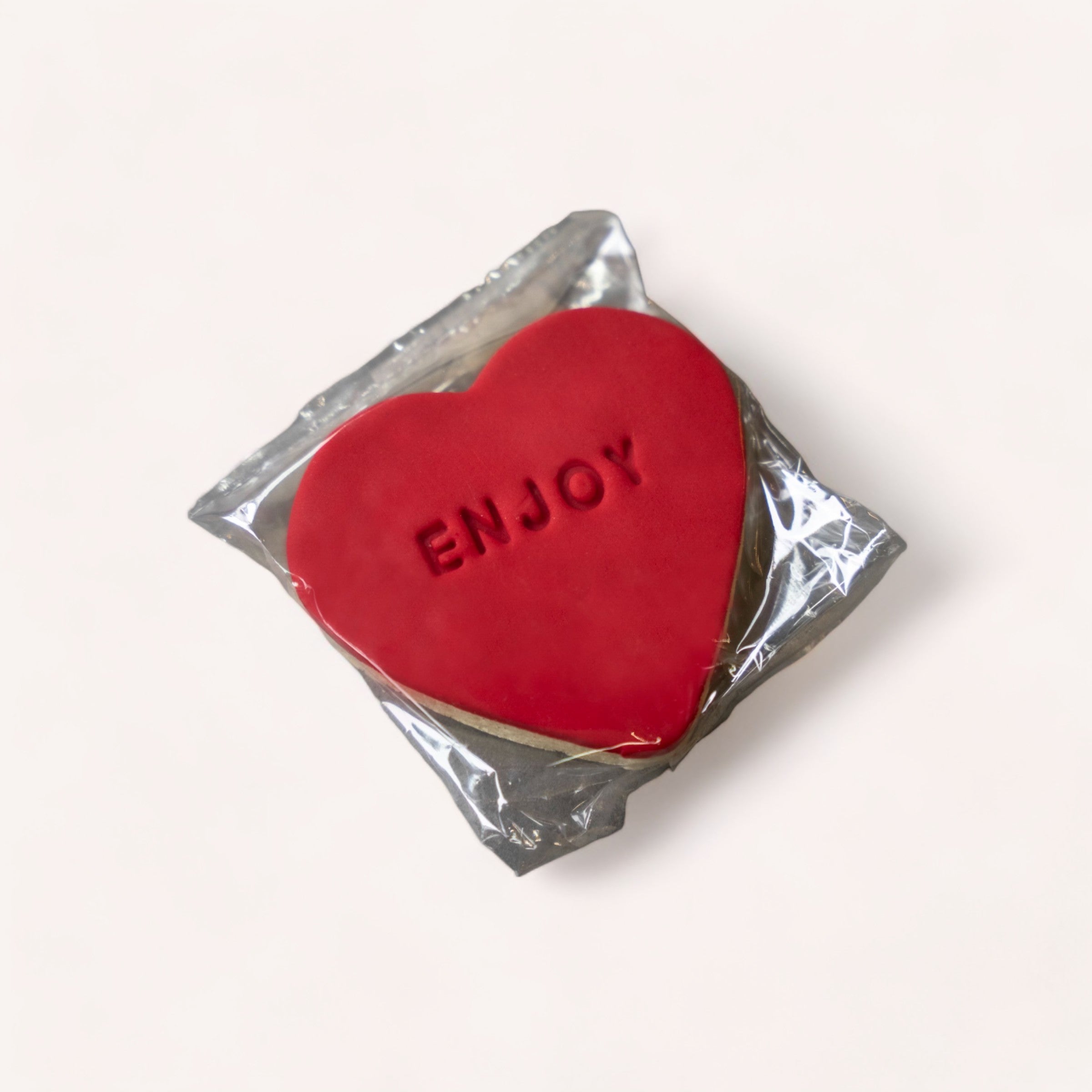 A heart-shaped red candy with the word "enjoy" embossed on it, wrapped partially in silver foil against a soft white background, making it a heartfelt gift.
Product Name: Heart 'Enjoy' Cookie
Brand Name: The Cookie Collective