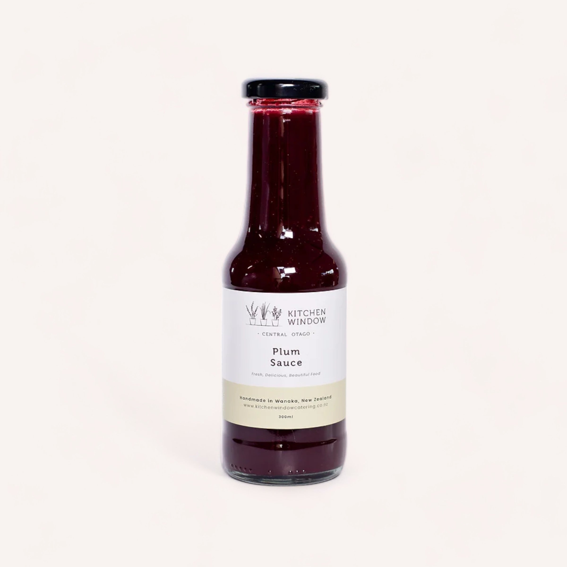 A bottle of award-winning Plum Sauce by Kitchen Window made with Black Doris plums from New Zealand on a solid light background, showcasing the product label with the brand "Kitchen Window" and flavor text indicating its.
