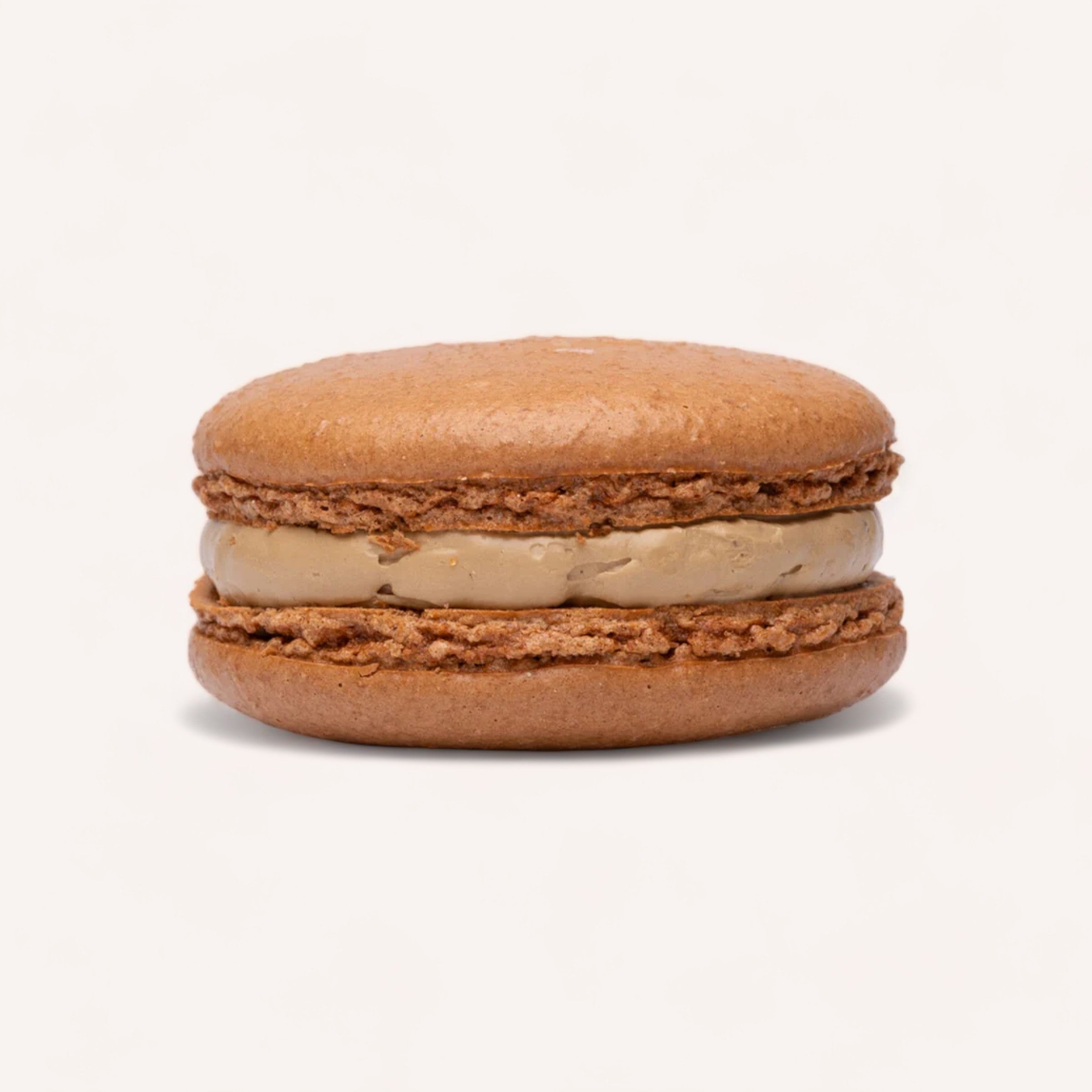 A single brown handmade Box of 12 Macarons by J'aime les Macarons with a creamy filling, isolated against a white background.