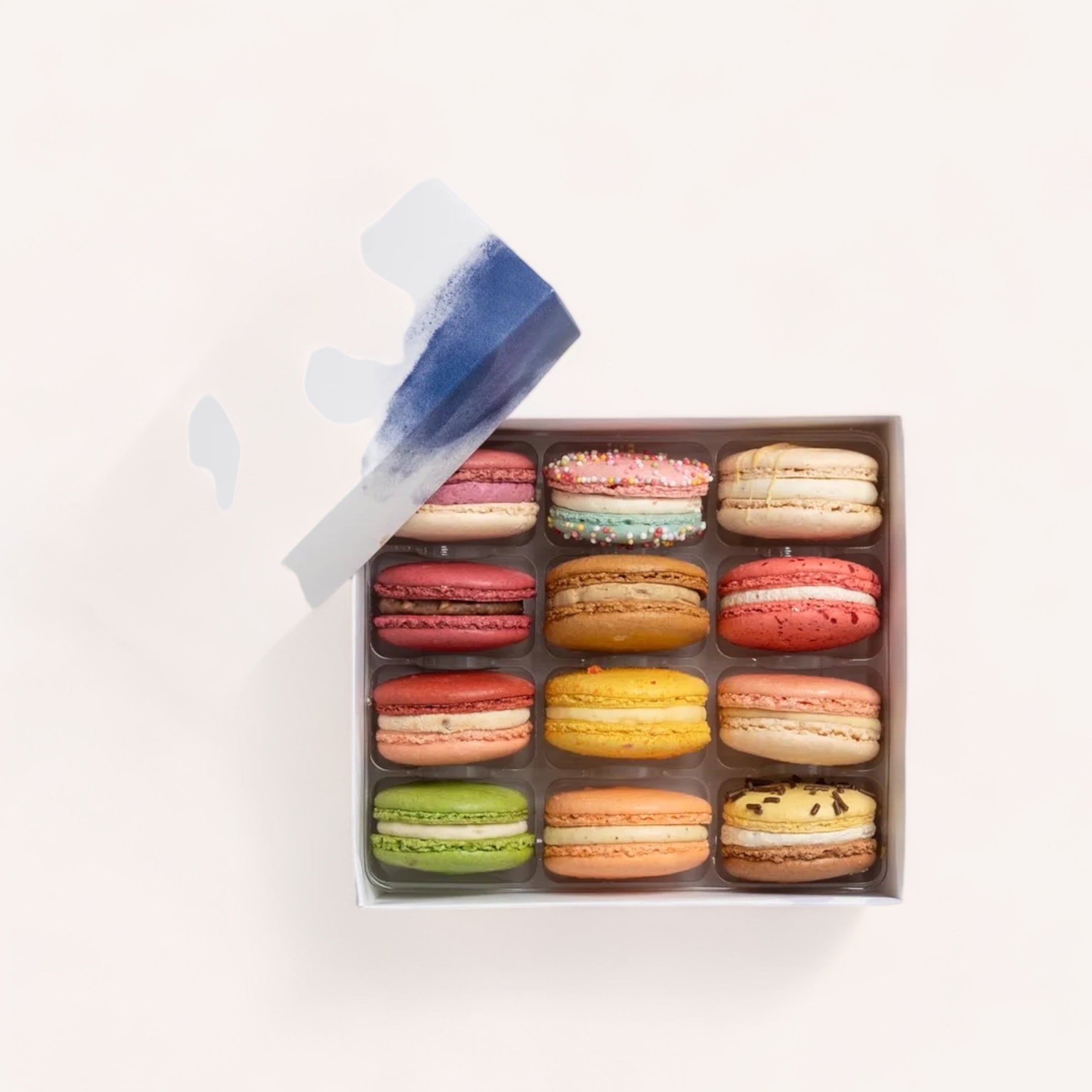 An assortment of colorful, handmade macarons from Christchurch, New Zealand, neatly arranged in a Box of 12 Macarons by J'aime les Macarons with the lid partially open, showcasing a tempting variety of flavors.