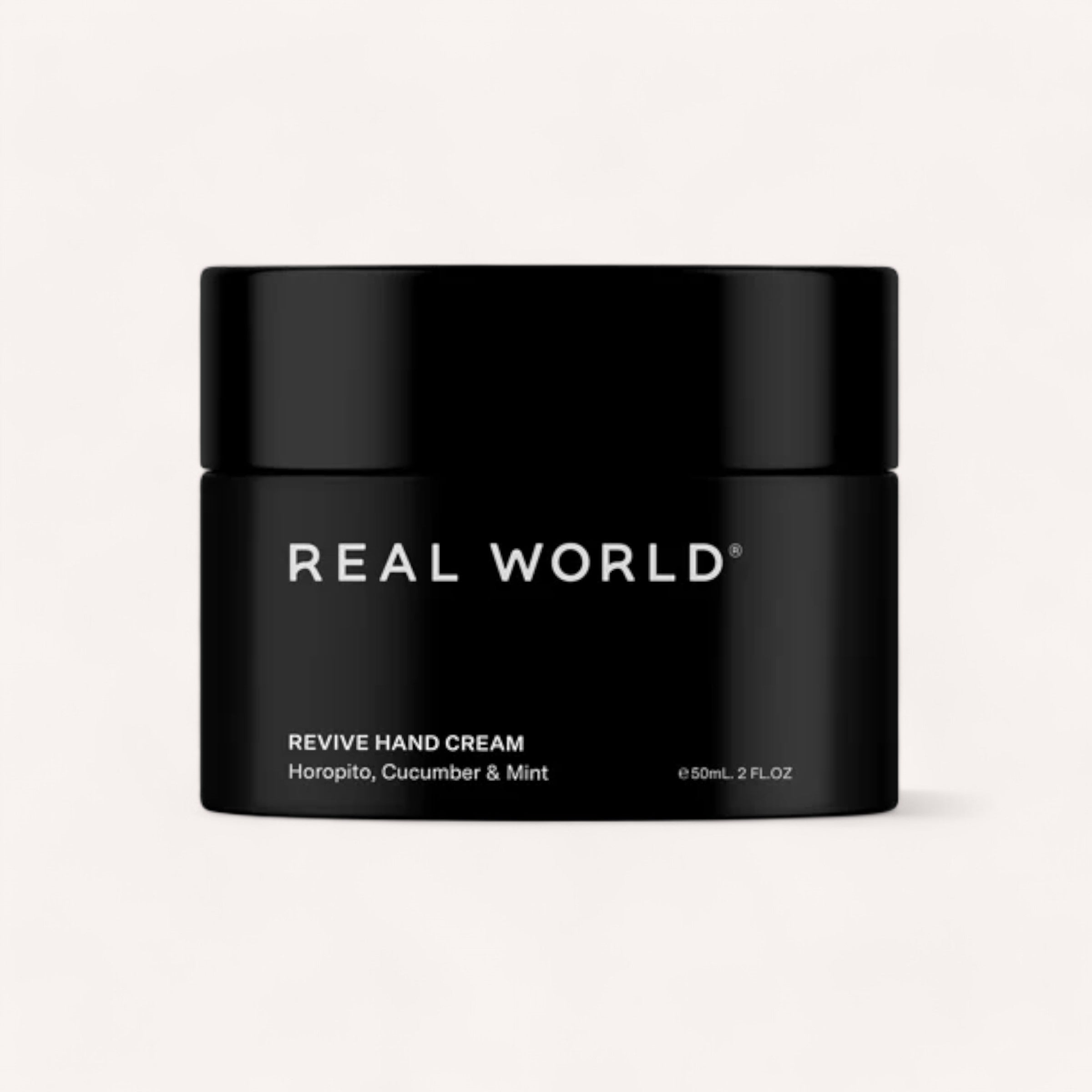 A black cylindrical container of Hand Cream by Real World is shown against a light background. The label displays the brand name "REAL WORLD" in white, uppercase letters, followed by "Revive Hand Cream" and "Horopito, Cucumber & Mint" in smaller text. This natural hand cream from New Zealand comes in a 50ml or 2 fl oz container.