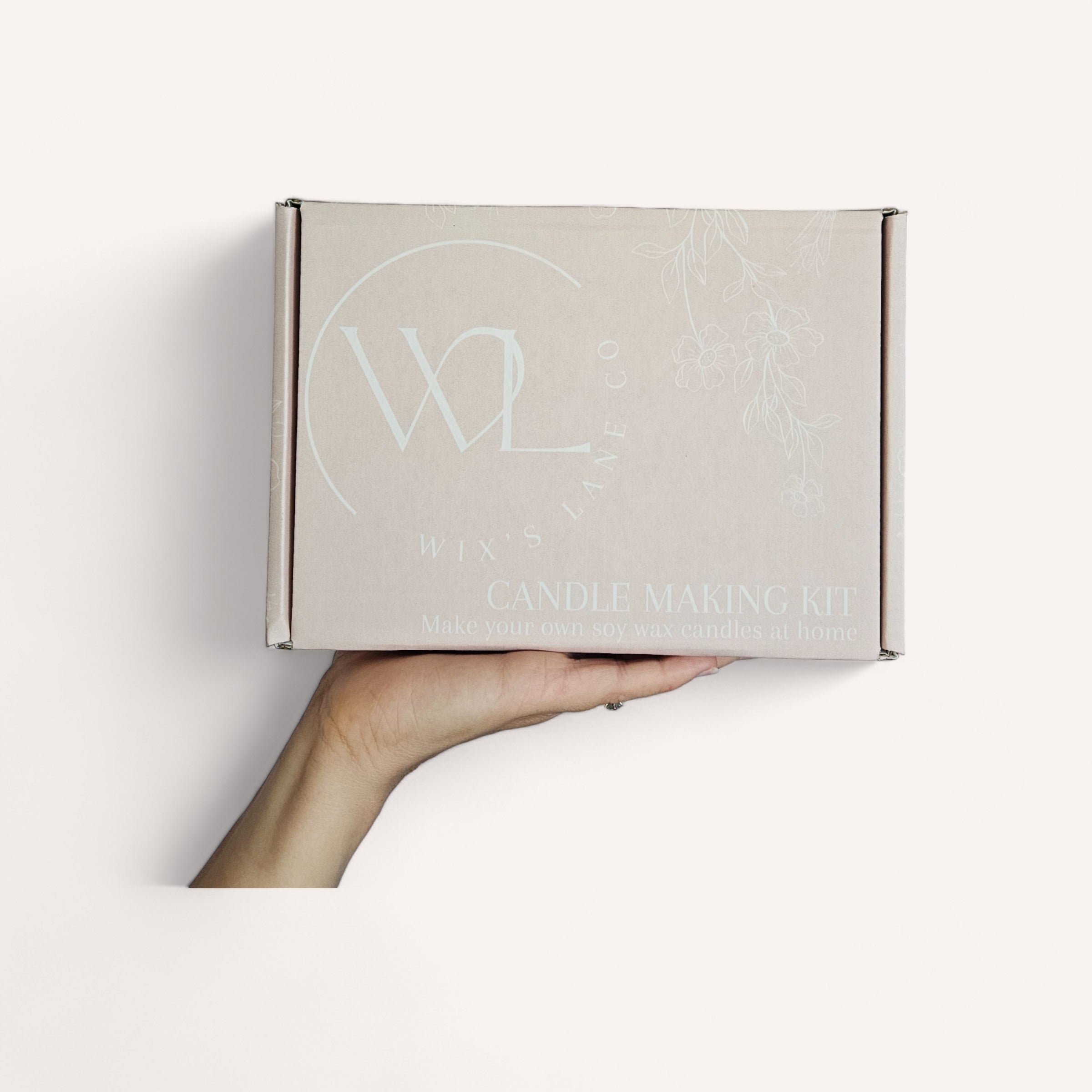 A hand presenting a Candle Making Kit by Wix's Lane Co. box with candle making instructions against a white background.