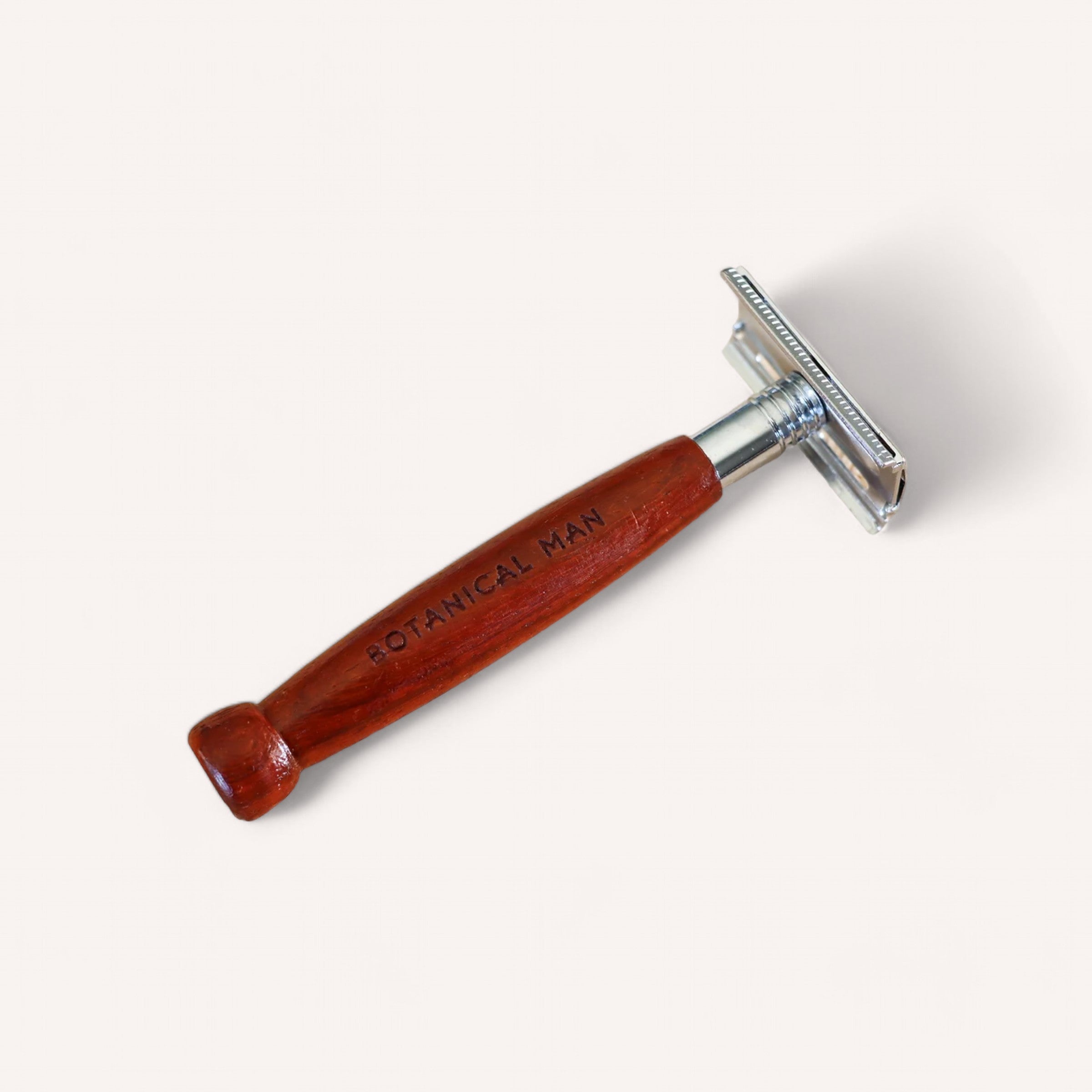 A beautifully crafted safety razor featuring a polished rosewood handle and a metallic blade head. The handle is elegantly engraved with the text "BOTANICAL MAN." Set against a plain, white background, it showcases the sleek and classic design of the Botanical Man Shaving Set by Botanical.