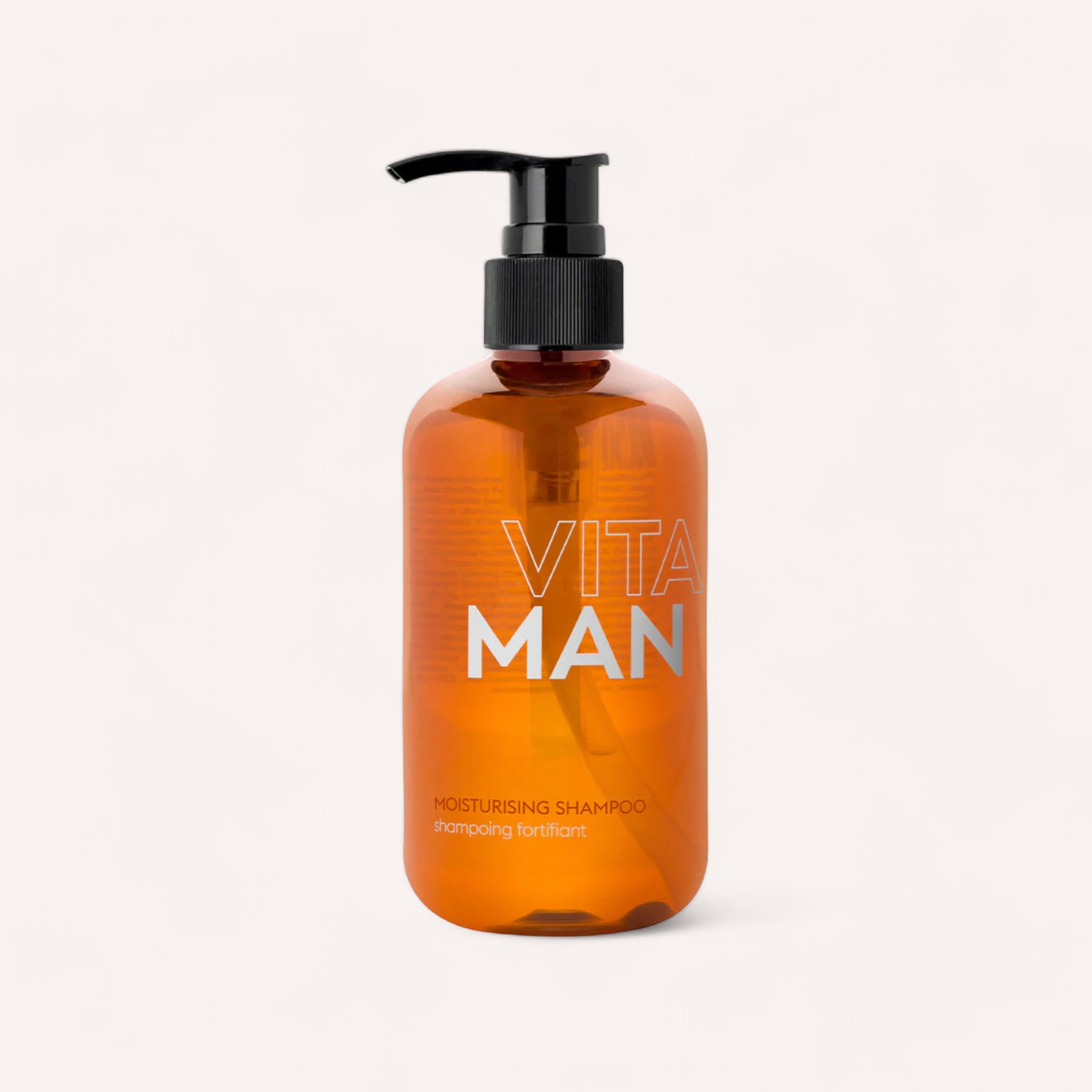 A translucent amber bottle with a black pump dispenser, labeled "Vitaman," contains Shampoo by Vitaman, a moisturising shampoo for healthy hair. The minimalist design features text in white and orange typography that reads, "Moisturising Shampoo" and "shampoing fortifiant.