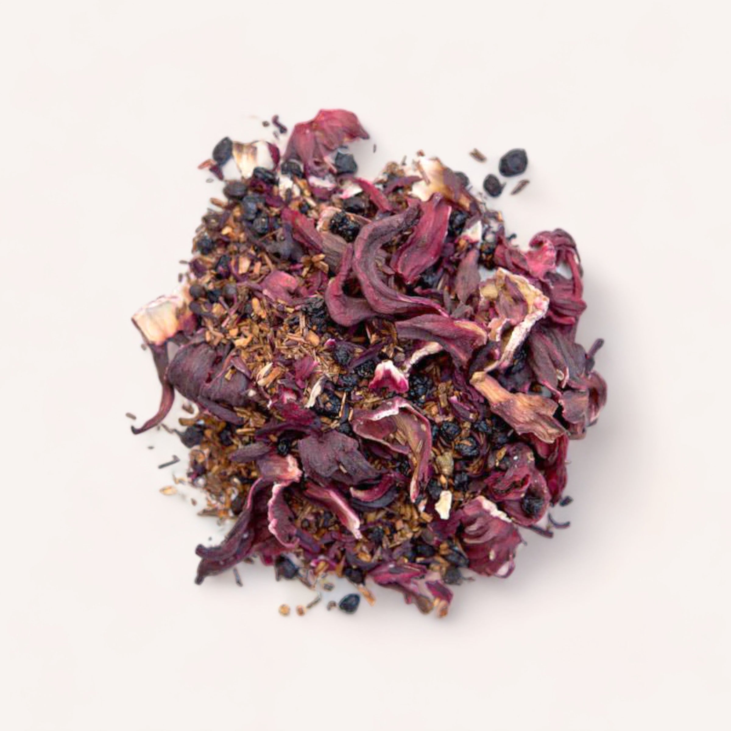 A pile of loose-leaf Bloom Tea by Forage + Bloom with dried rose petals, various herbs, and antioxidant-rich hibiscus tea on a light background.