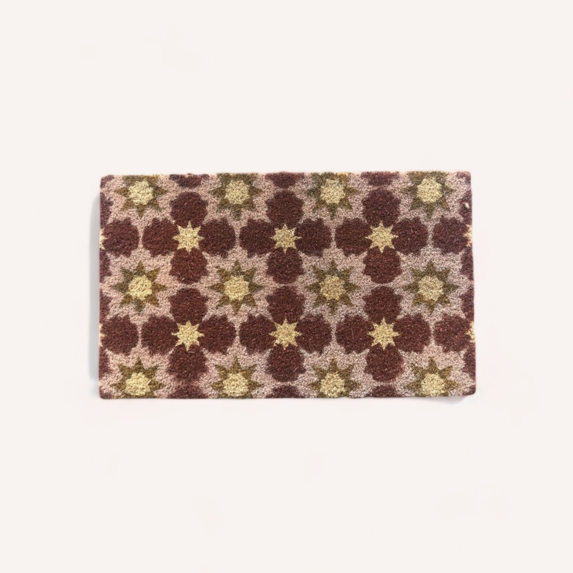 The Doormat by Potted NZ from Potted NZ is a rectangular, plush coir door mat measuring 45 x 70 cm. It features a repeating pattern of interlocking floral shapes in brown and light green, set against a plain white background. The design showcases intricate, symmetrical flower motifs that create a rich, textured look and it comes complete with rubber backing for durability.