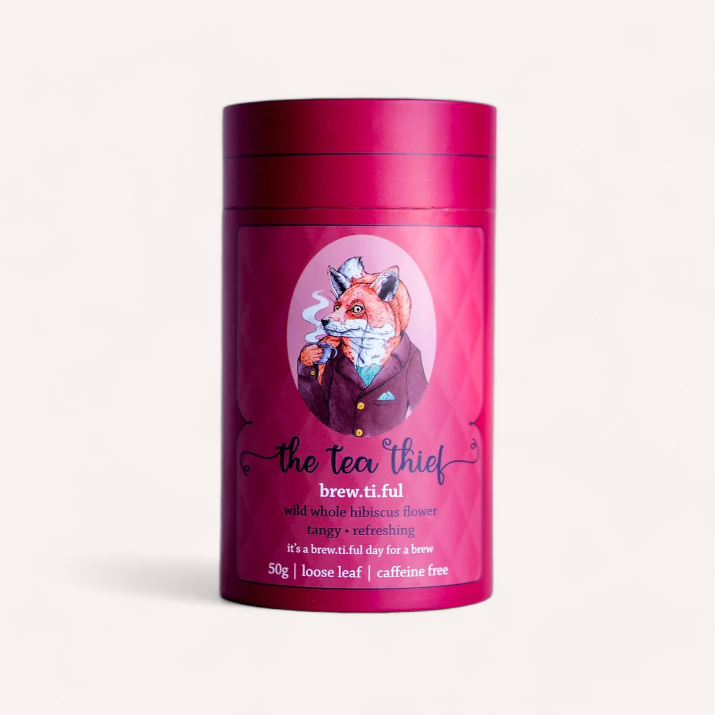 A light cream cylindrical tea canister from The Tea Thief brand showcases an illustration of a fox in formal attire. The magenta label reads "Tea by The Tea Thief" and "brew.ti.ful," highlighting award-winning, New Zealand-brewed caffeine-free tea comprised of tangy and refreshing wild whole hibiscus flowers, available in a 50g loose leaf format.