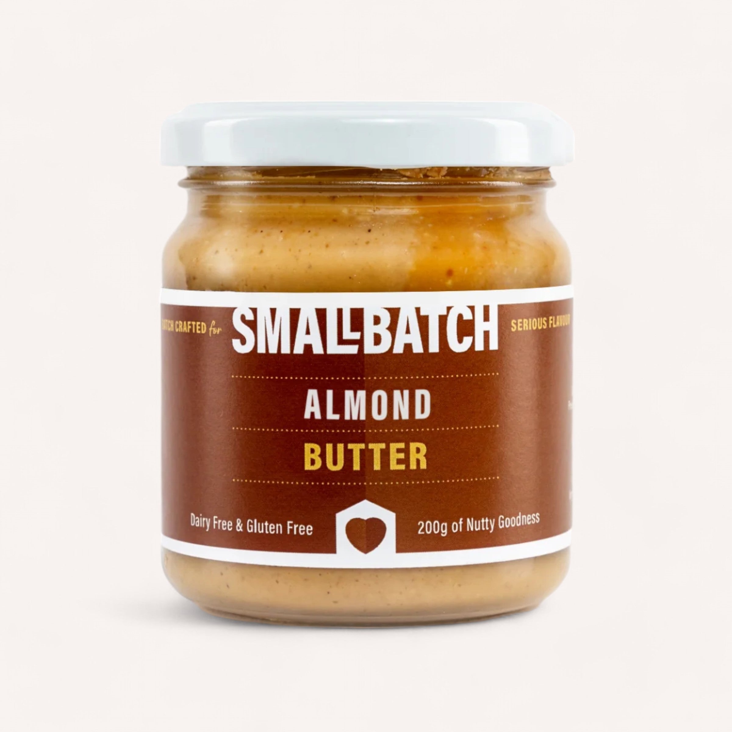 A jar of Almond Butter by Smallbatch comes with a white lid and a brown label prominently displaying "Small Batch" in large white letters, along with "Almond Butter." It emphasizes being "Dairy Free & Gluten Free" and contains "200g of Nutty Goodness," crafted from roasted Australian almonds. The background is a plain light hue.