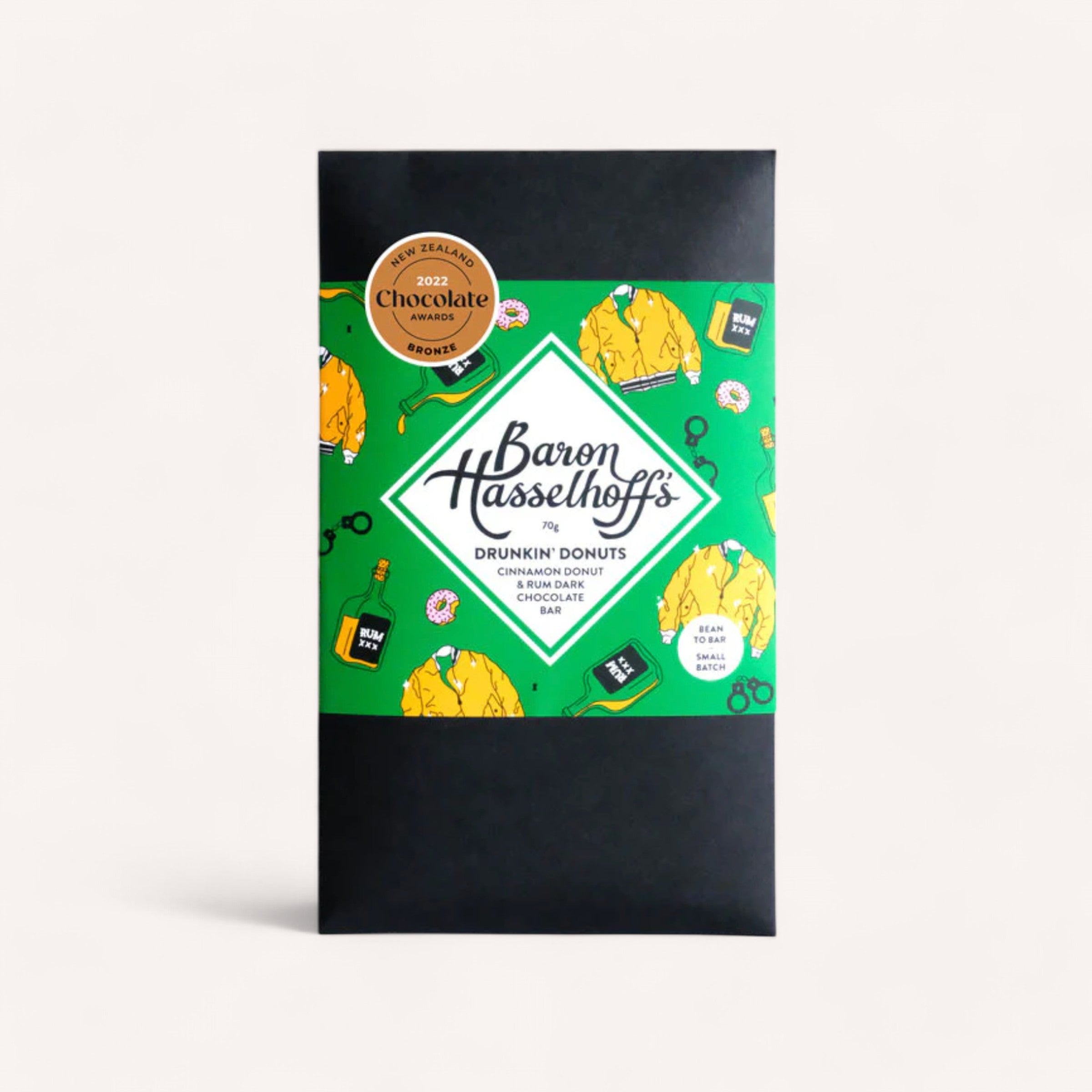 A black chocolate bar package designed with a green label adorned with playful donut illustrations suggests the flavor of cinnamon donut. The label displays "Drunk'n Donuts by Baron Hasselhoff's," while a gold-colored award sticker in the upper left corner highlights its win at the 2022 NZ Chocolate Awards.