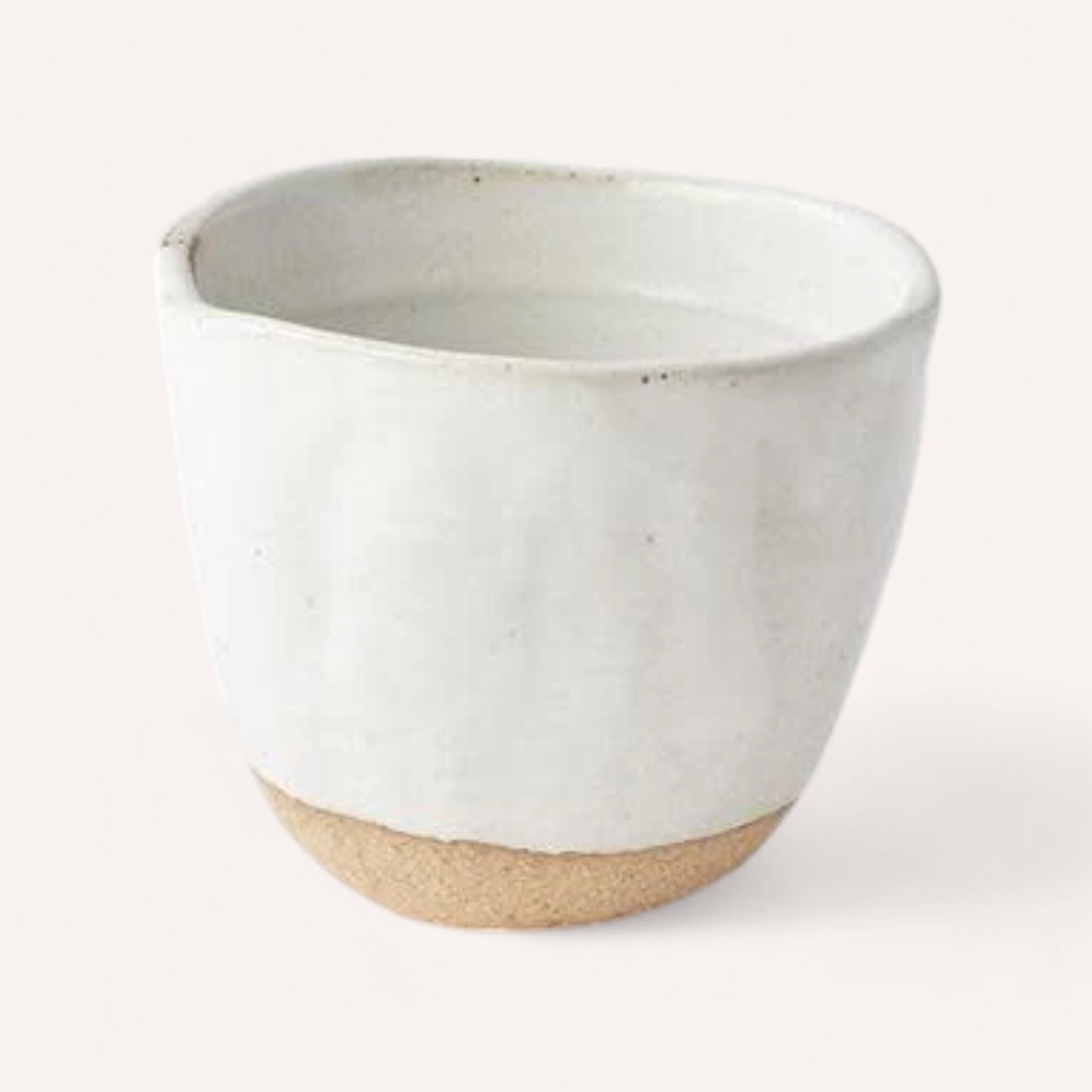 Introducing the Handmade Ceramic Cup by Naibu, crafted from Minoyaki porcelain. This cup is elegantly designed with a smooth off-white glaze and features a natural, unglazed base. Its charming rustic and minimalist aesthetic is complemented by a small spout on one side. The backdrop sets the tone with its neutral, soft beige hue.