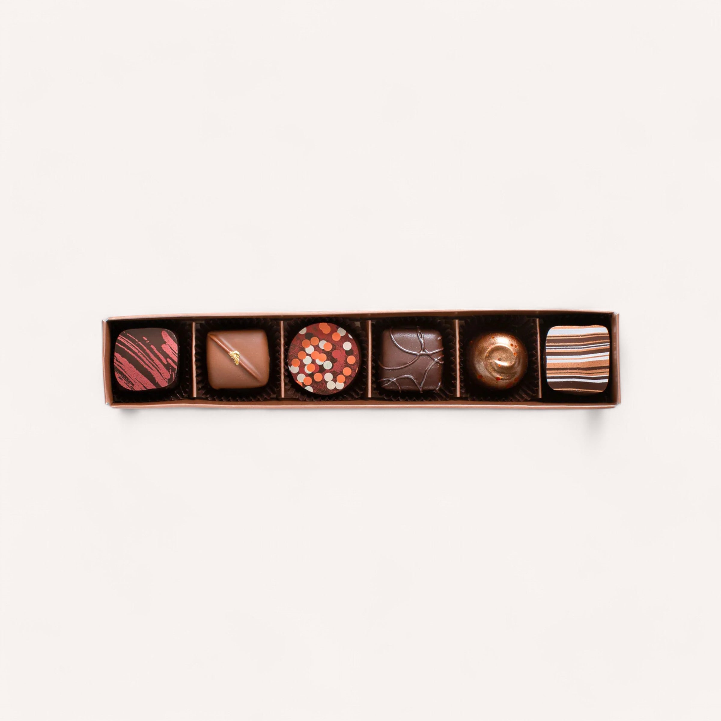 Displayed against a white background, Colestown's Box of 6 Chocolates showcases the brand's premium quality. The hand-made assortment includes distinct designs: red stripes, a smooth caramel square, bright circular sprinkles, cracked dark chocolate texture, and a piece with a swirl on top, all neatly arranged in an elegant brown box.