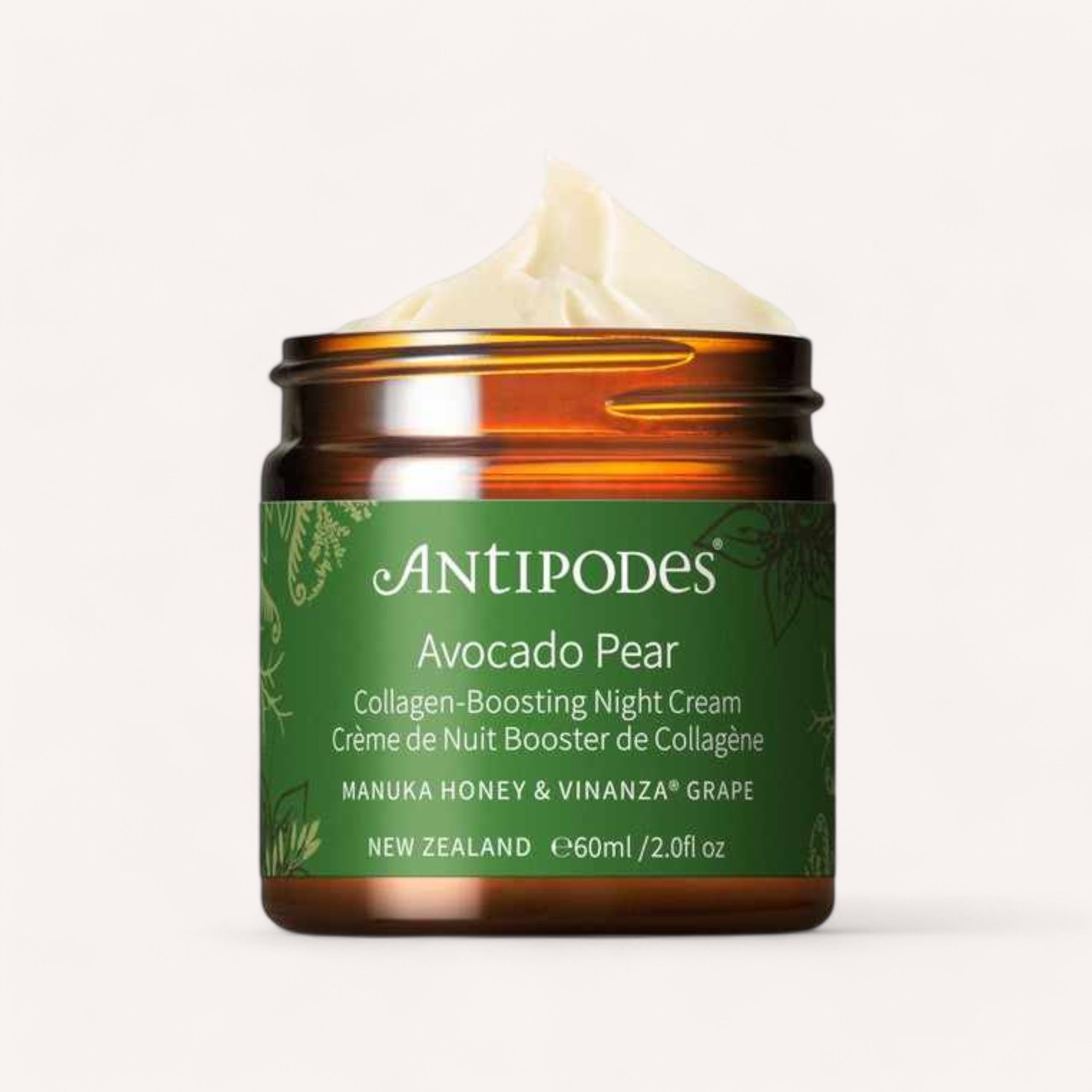 A jar of Avocado Pear Night Cream by Antipodes is elegantly displayed, highlighting its amber design and green label. Enriched with collagen-boosting manuka honey and vinanza grape, the visible swirl of cream promises nourishment. This 60ml or 2.0fl oz product is proudly made in New Zealand.