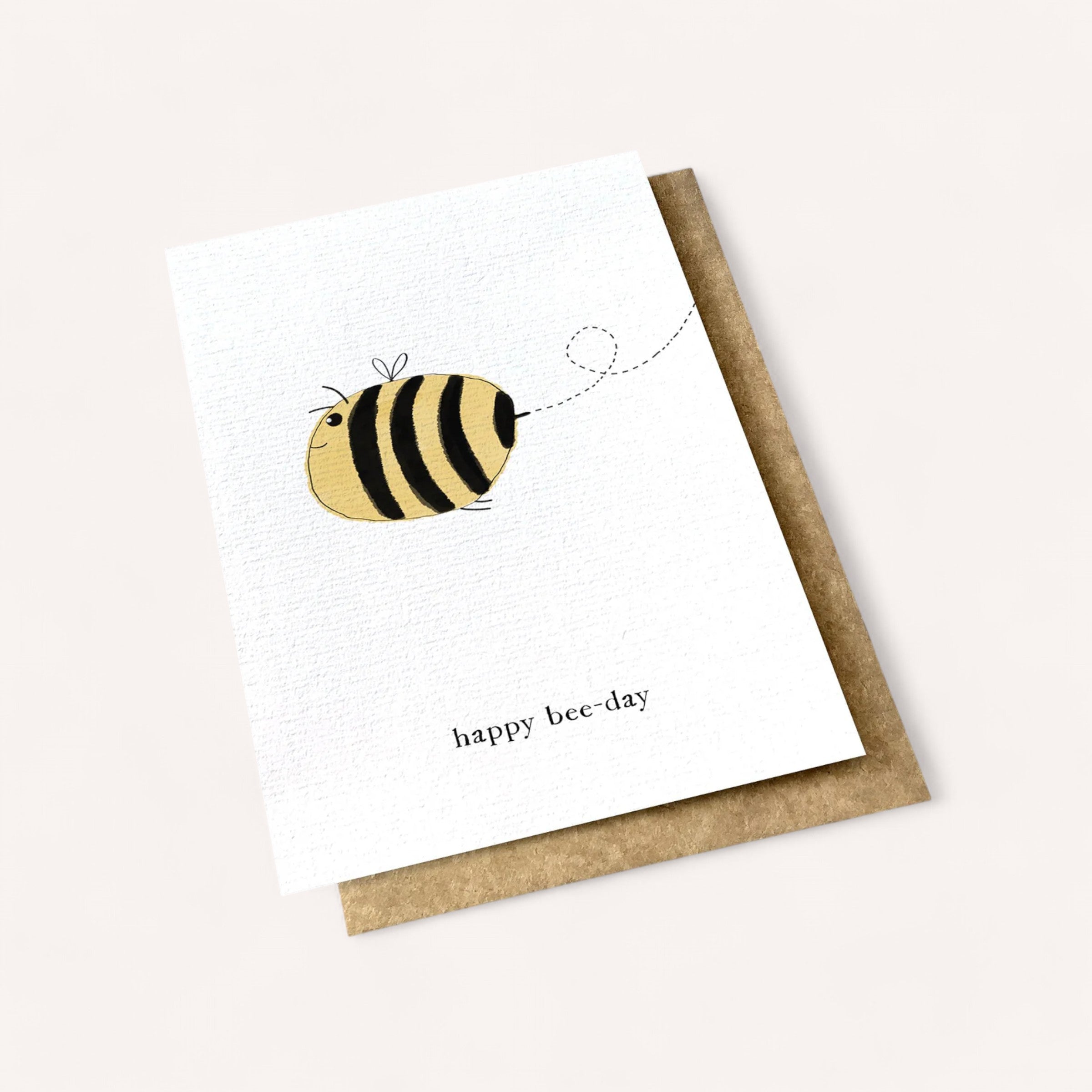 The Happy Bee-Day Card by Ink Bomb showcases an adorable cartoon bee adorned with black and yellow stripes, small wings, and a dashed line to illustrate its flight path. Underneath the bee illustration, you’ll find "happy bee-day" inscribed. The card is paired with a brown envelope and set against a white backdrop, while the inside is left blank for your personal message.