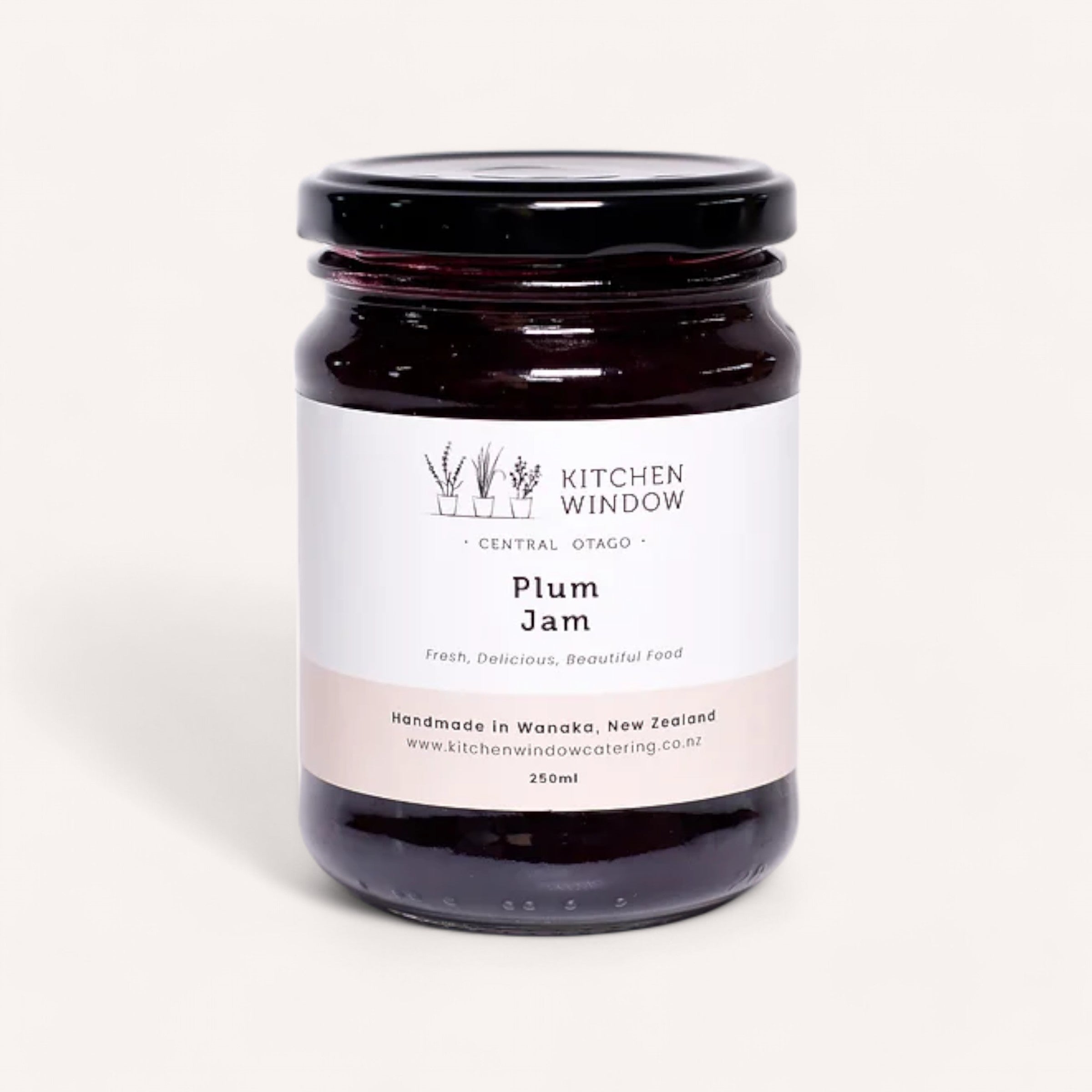 A 250 ml glass jar of Plum Jam by Kitchen Window, topped with a black lid, features a minimalist label adorned with a plant illustration and the phrases "Plum Jam" and "Handmade in Wanaka, New Zealand." This delicious jam is crafted from the finest Black Doris plums from Central Otago.