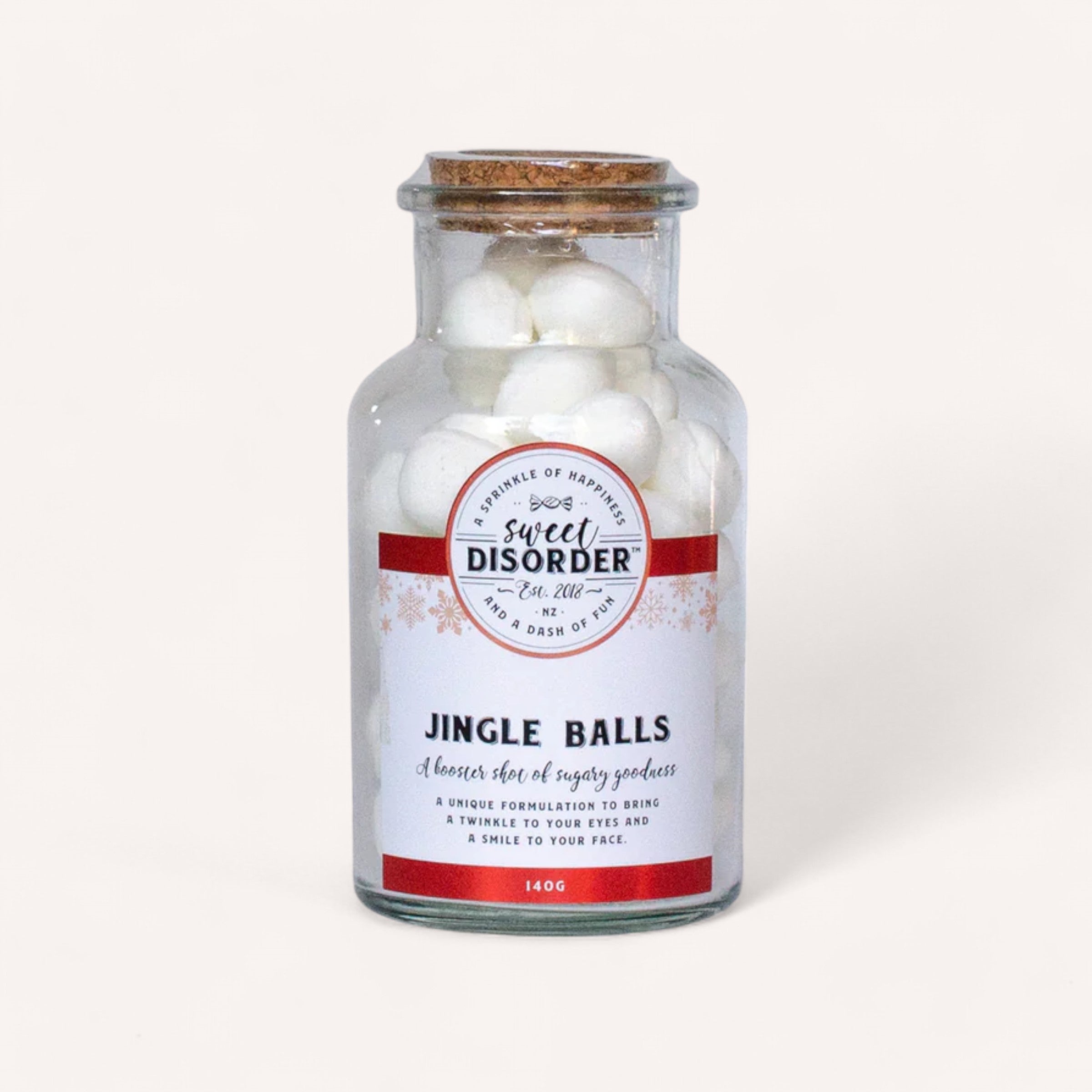 A small glass jar with a cork lid labeled "Sweet Disorder" contains Jingle Balls Lollies, which are white spherical candies similar to festive Granny mints. Decorated with snowflakes and the playful title, the jar holds 140g of New Zealand's unique formulation and features a vibrant red and white label.