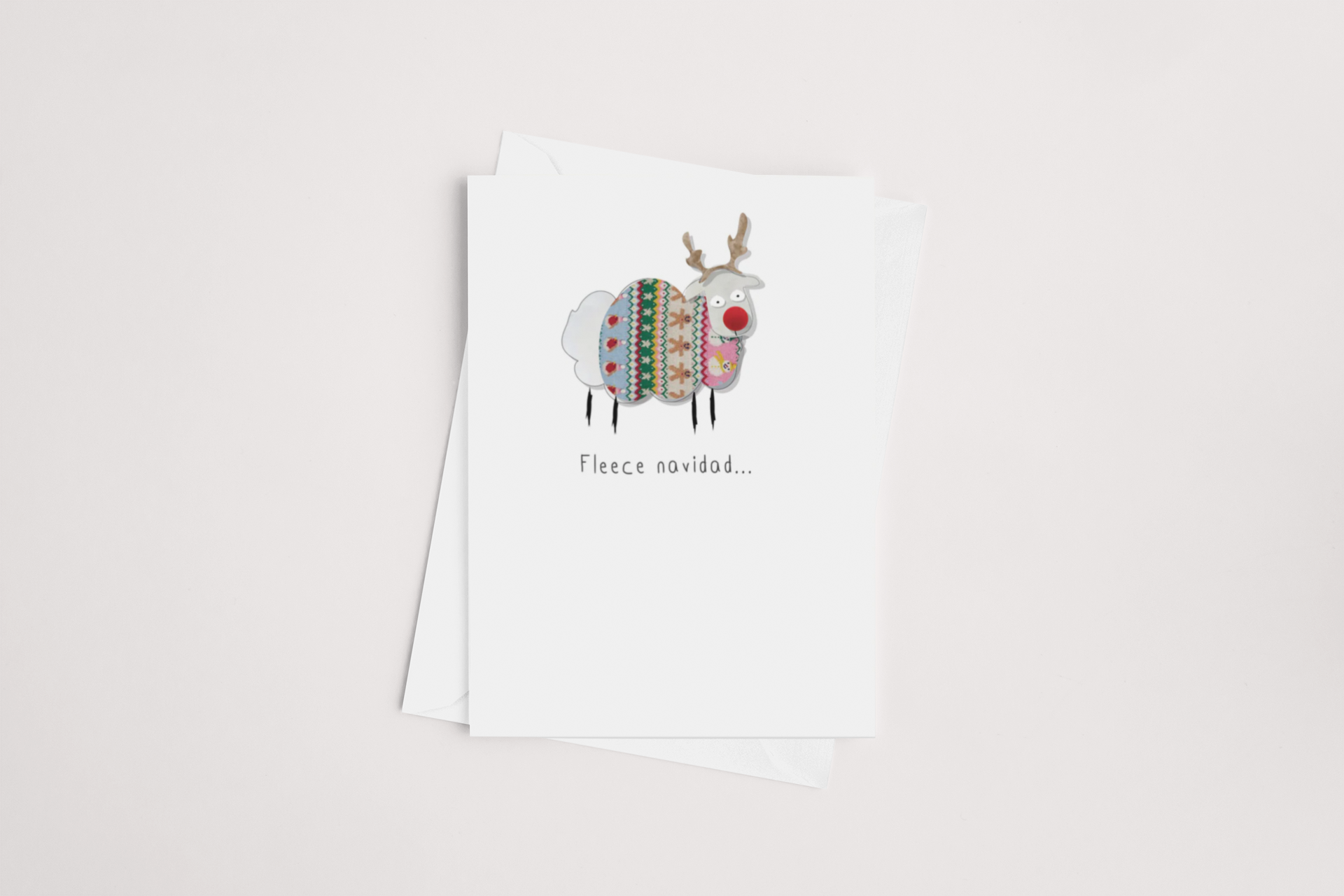 The Fleece Navidad Christmas Card by iCandy features a cartoon sheep with antlers, resembling a reindeer, wearing a vibrant sweater. Beneath the illustration, it says "Fleece navidad..." The card is slightly open on a white envelope against a neutral background and is blank inside, making it ideal for any occasion.