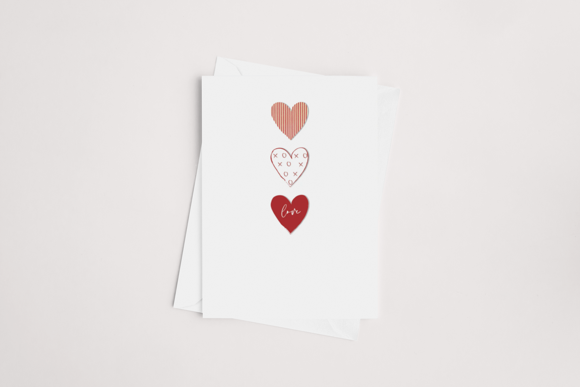 The "Three Tier Love Hearts Card" by iCandy features a design of three hearts on a white background: one striped in pink, another displaying "XOXO" on white, and a third with the word "love" in cursive red. It is blank inside, allowing for your personal message. A partially visible white envelope accompanies the card.