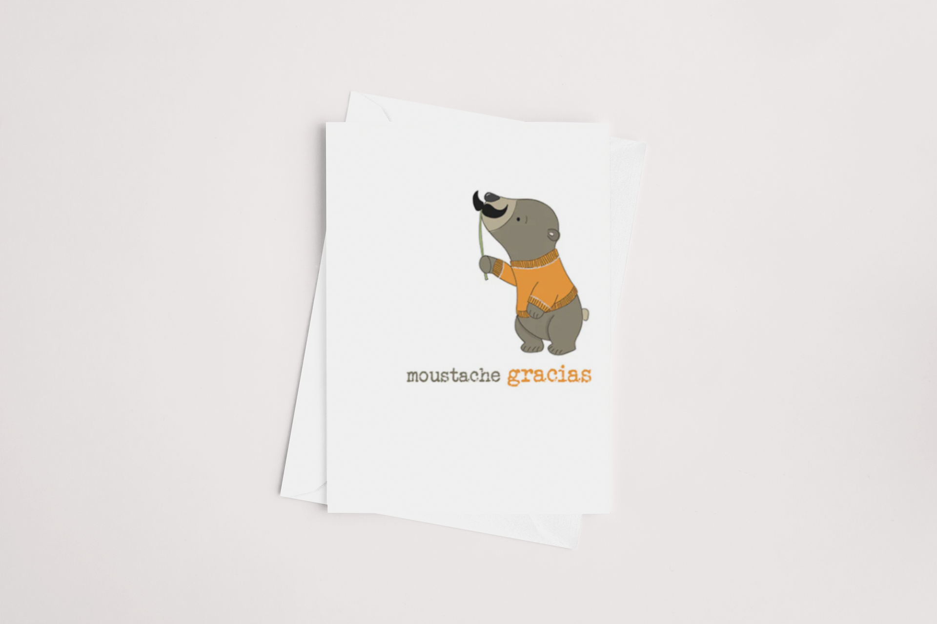 The Dandelion "Moustache Gracias Thank You Card" showcases a whimsical cartoon sloth wearing an orange sweater and playfully holding a black mustache on a stick. The phrase "moustache gracias" is printed below the illustration. This charming card comes with a blank interior and includes a brown envelope, plus it qualifies for Multibuy offers.