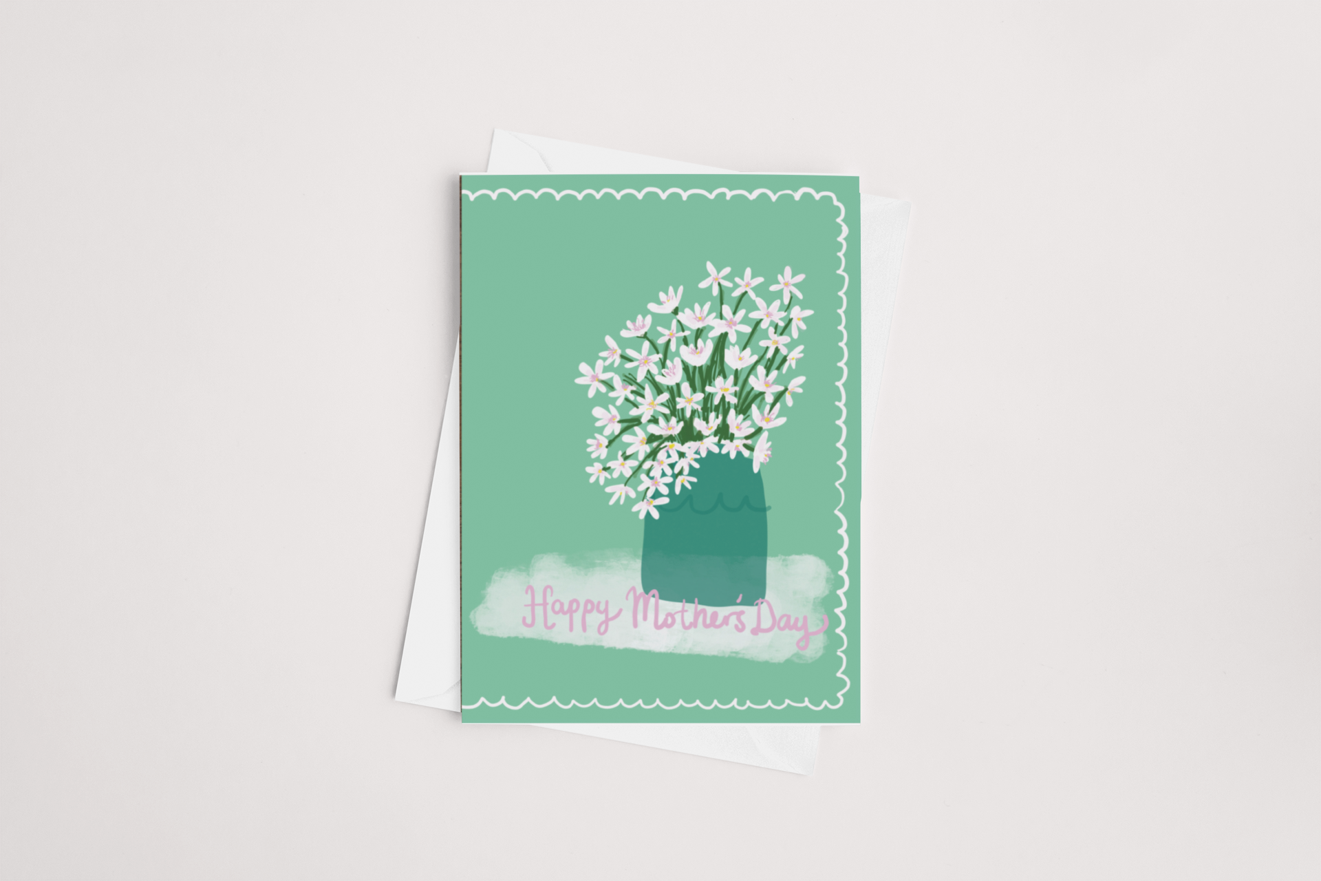 A Sweet Pea Creations Floral Mother's Day Card with a teal background and white flower design, overlaying text "Happy Mother's Day," placed on a white surface with an envelope underneath.