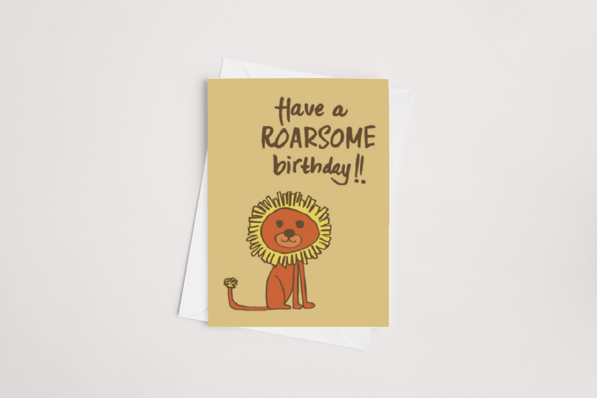 The "Roarsome Birthday Card" by Tuesday Print showcases a cartoon lion with a cheerful expression and mane on a tan background. The playful text at the top reads, "Have a ROARSOME birthday!!" Blank inside for your personalized message, this card is paired with a white envelope and displayed on a light surface.