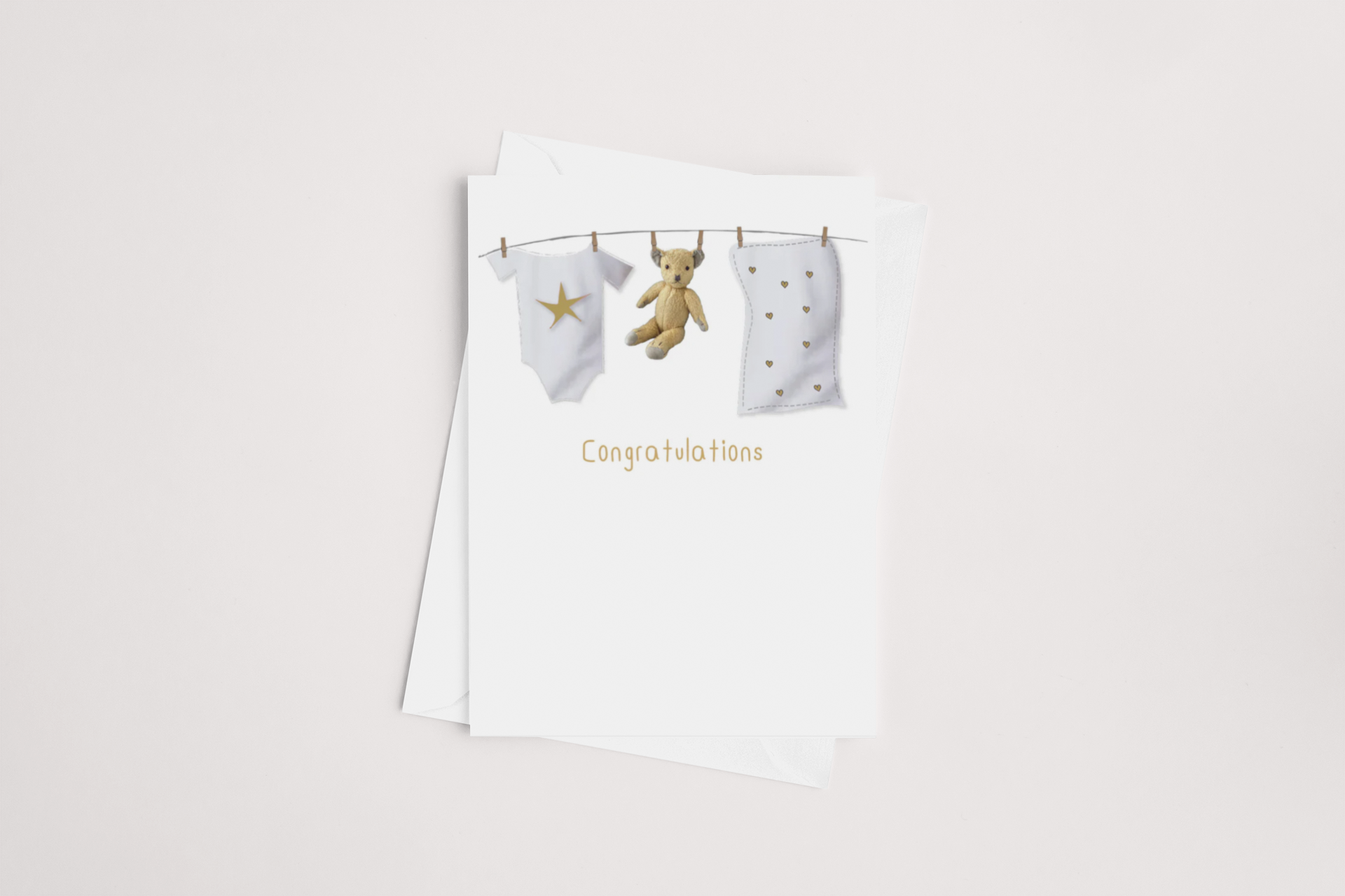 The Baby Washing Line Card by iCandy showcases a minimalist design with baby clothes, a teddy bear, and a blanket hanging on a clothesline. Beneath the imagery, "Congratulations" is elegantly printed in orange. The card is blank inside for your personalized message and comes with a white envelope set against a soft, neutral background.