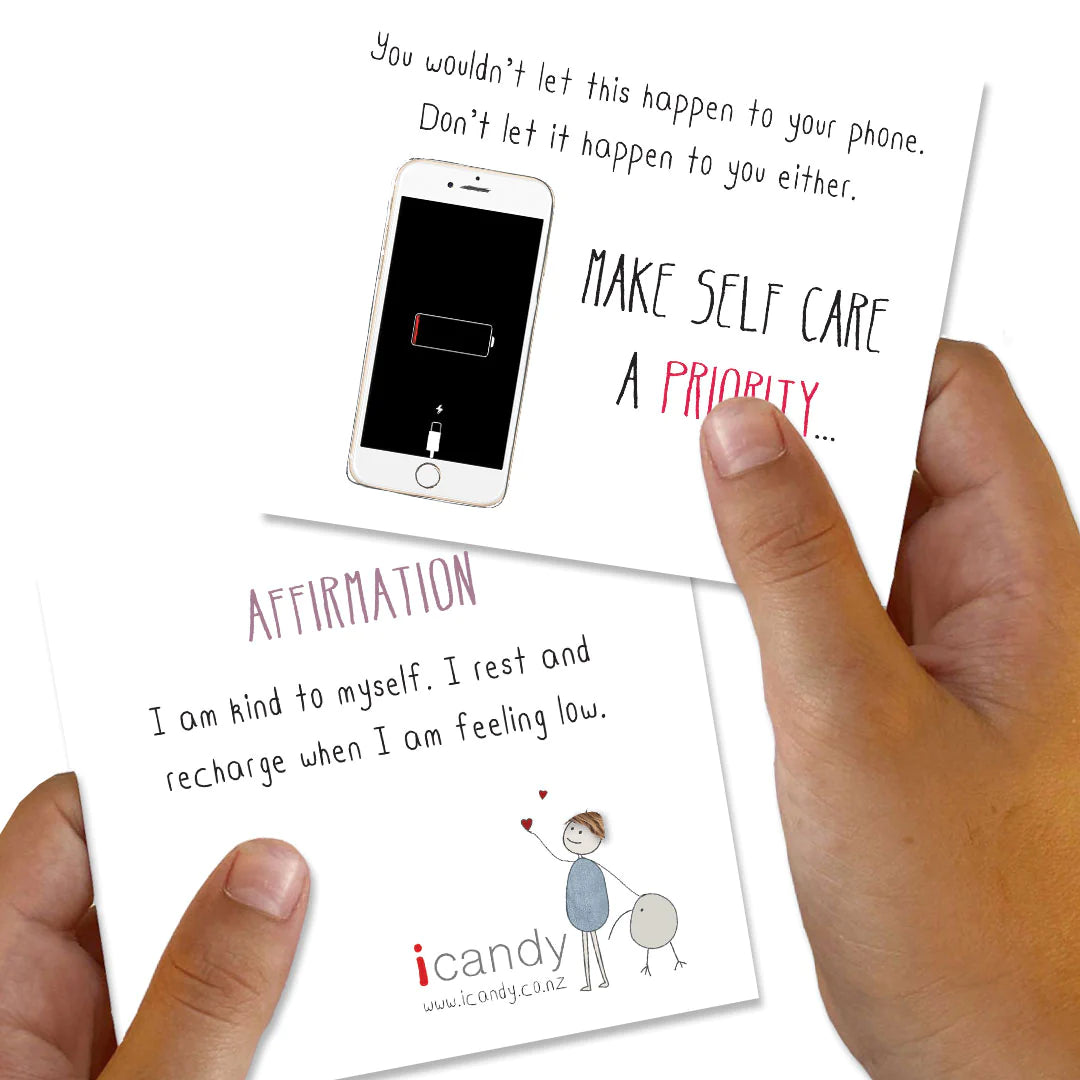 Two hands holding two cards. The top card shows a phone with a low battery and text: "You wouldn’t let this happen to your phone. Don’t let it happen to you either. Make self-care a priority for positive headspace with the Positivity Pack from iCandy..." The bottom card reads: "Affirmation: I am kind to myself. I rest and recharge when I am feeling low.