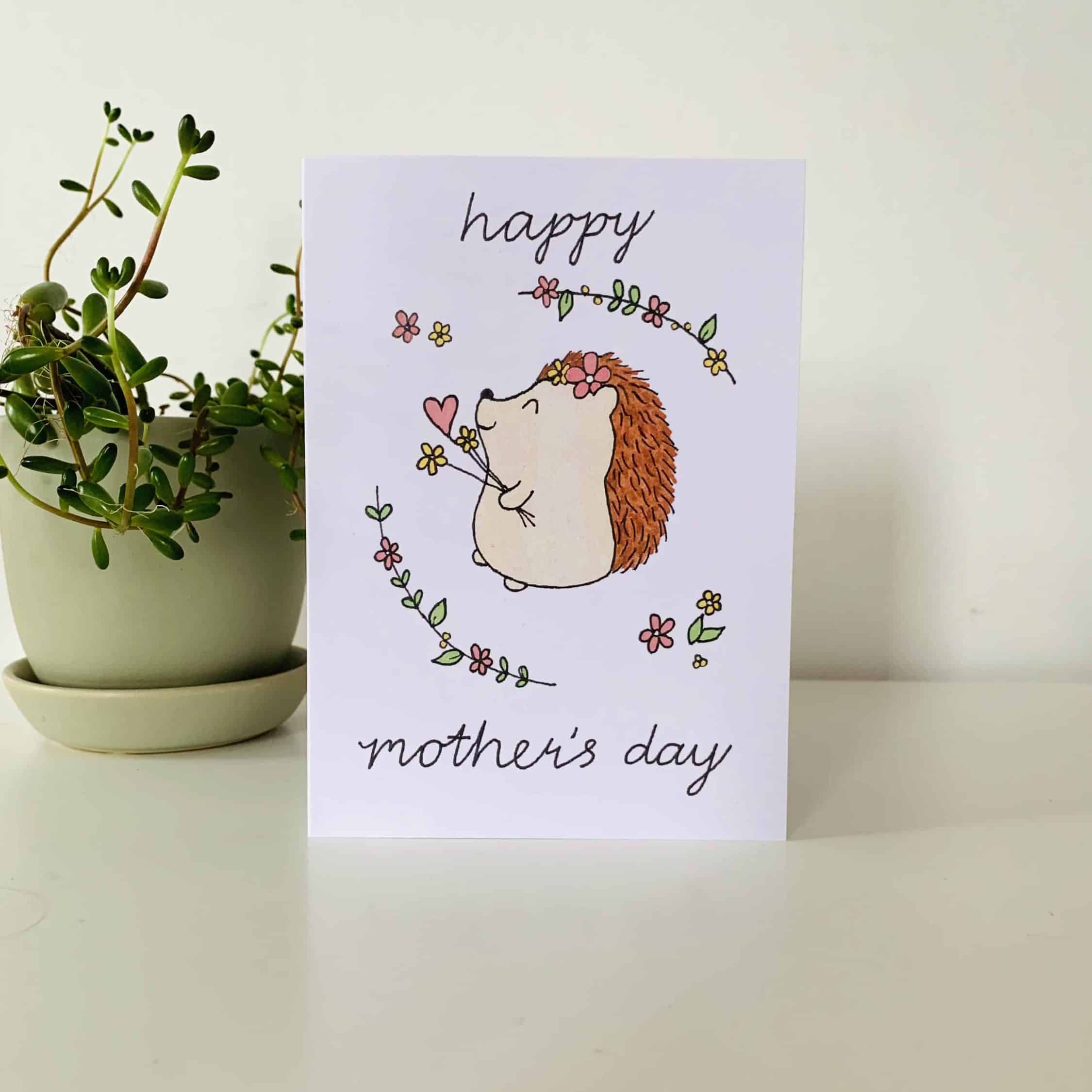 A Hedgehog Mother's Day Card from Sweet Pea Creations, decorated with an adorable illustration of a hedgehog surrounded by flowers, with the words "happy mother's day" written in a playful font.